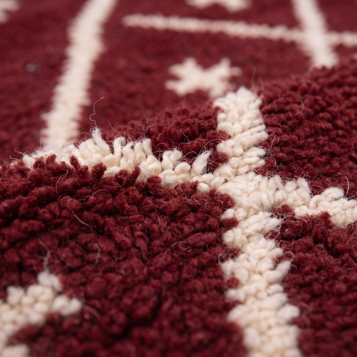 Gros plan sur un motif du tapis berbère Ammas, fond bordeaux à poil moyen dense