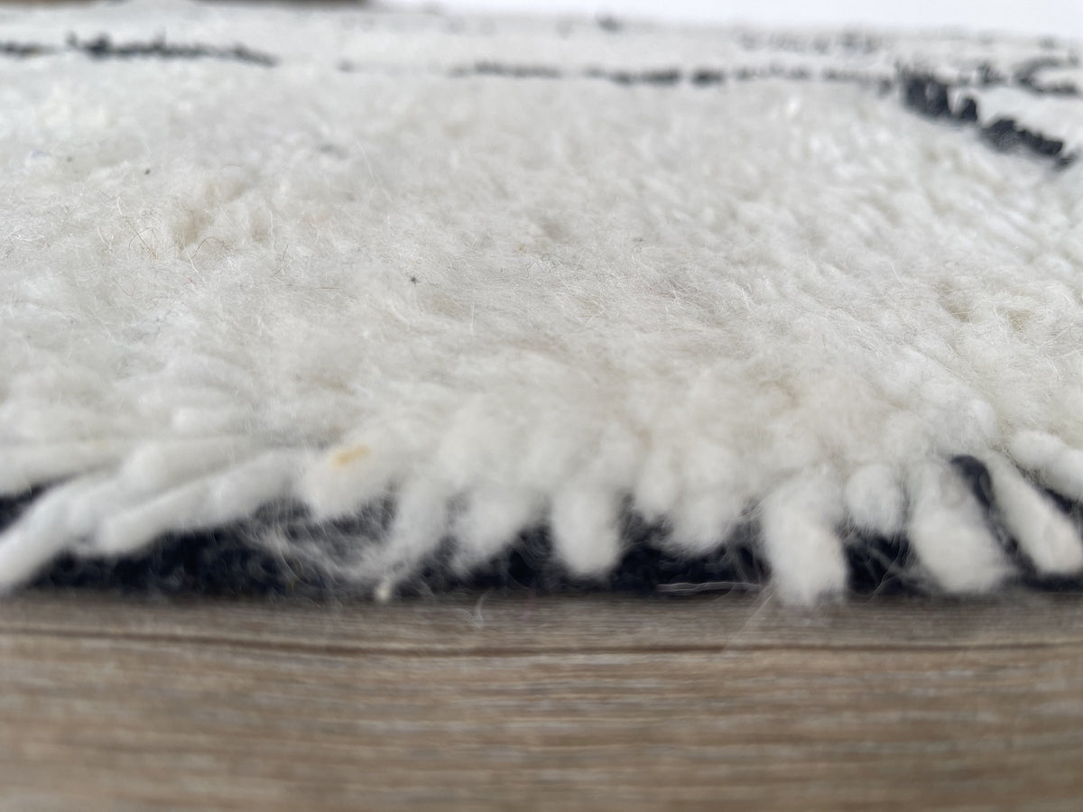 Gros plan sur le coin relevé du tapis berbère Ilzoun, épaisseur du poil long et dos tissé à la main