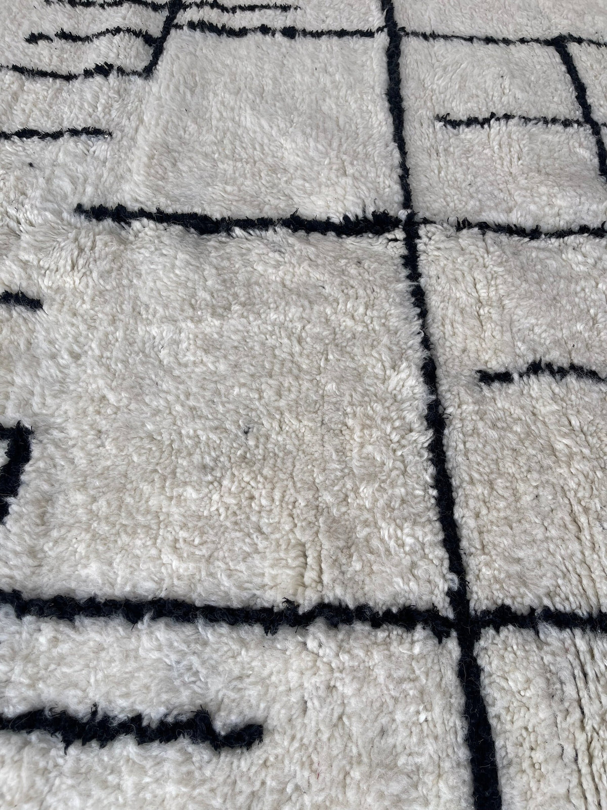 Gros plan sur la laine du tapis berbère Ilzoun, laine de mouton au poil long, noire et blanche