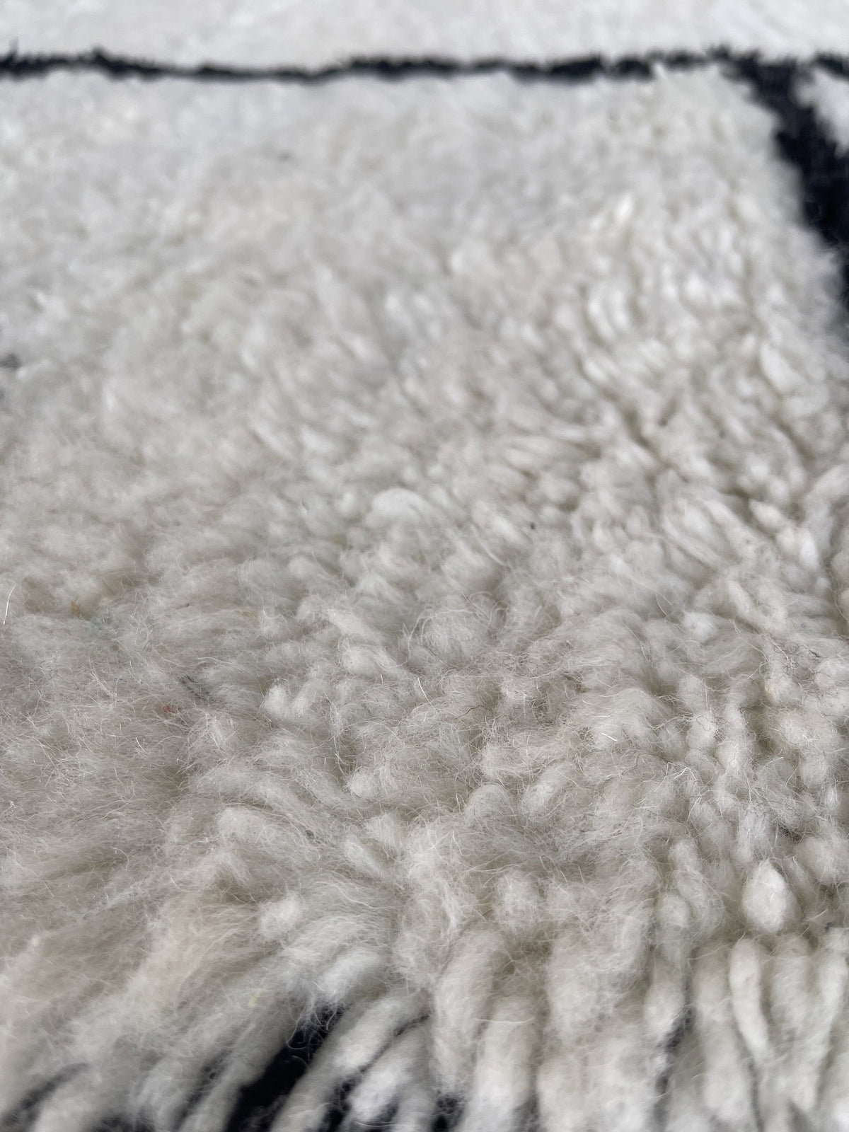 Gros plan sur la laine du tapis berbère Ilzoun, nœuds serrés et tracé du motif de près