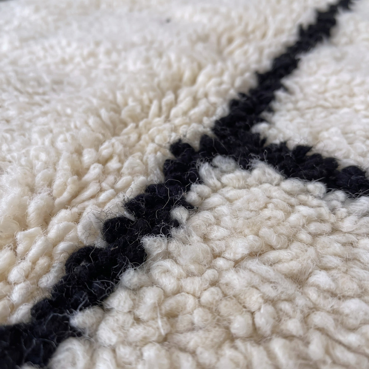 Gros plan sur un motif du tapis berbère Ilzoun, fond ivoire à poil long, en haut