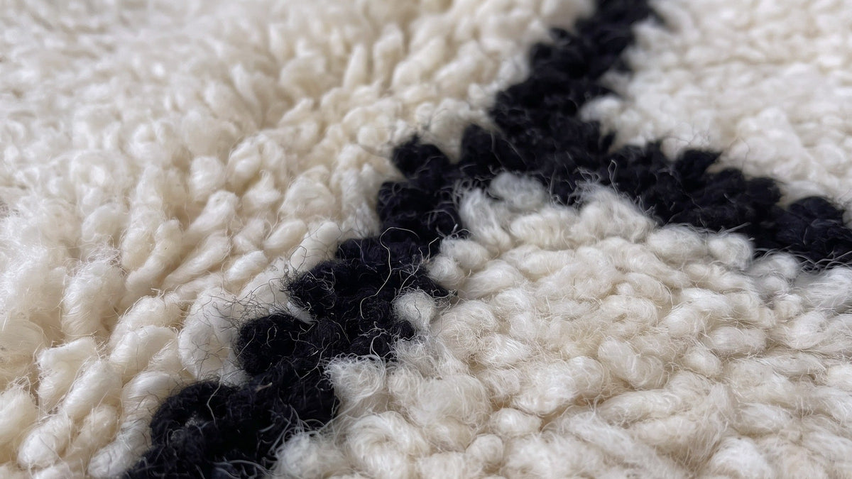 Gros plan sur la laine du tapis berbère Ilzoun, poil noir et blanc noué à la main