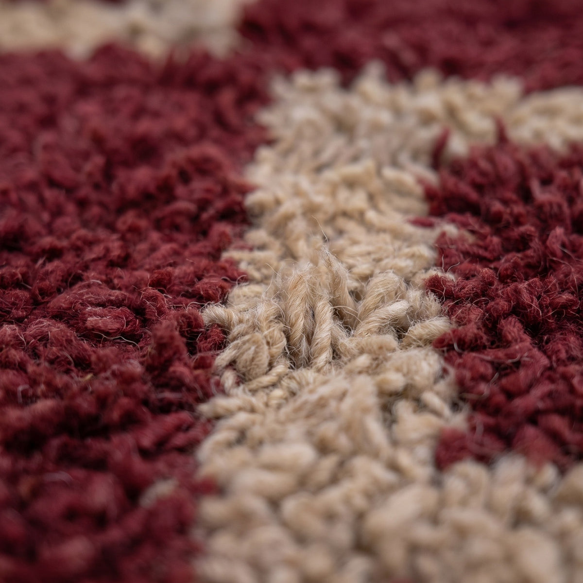 Gros plan sur un motif du tapis berbère Tigejdit, champ bordeaux poil long, quatre losanges beiges alignés