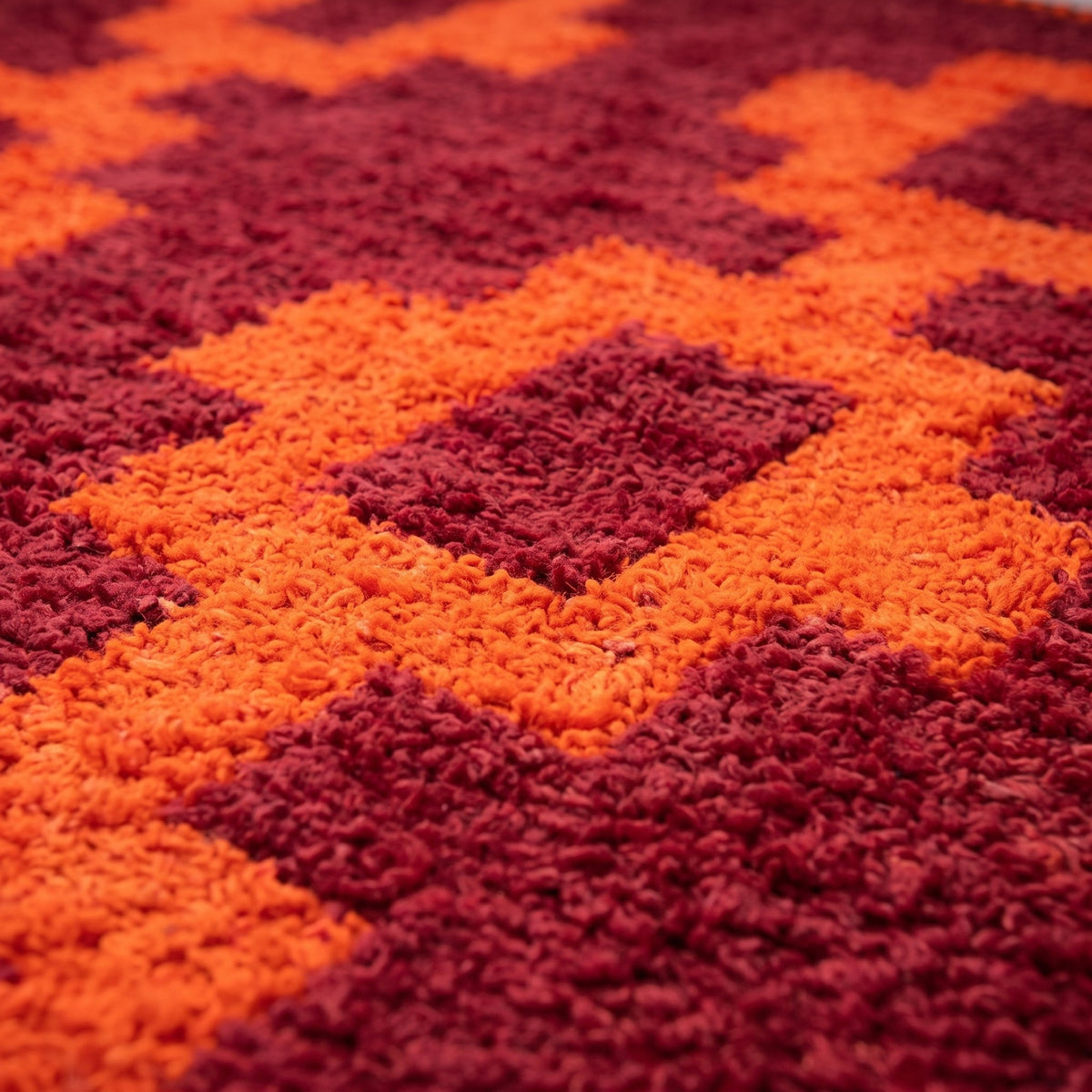 Gros plan sur un motif du tapis berbère Izem, fond bordeaux poil long, trois colonnes