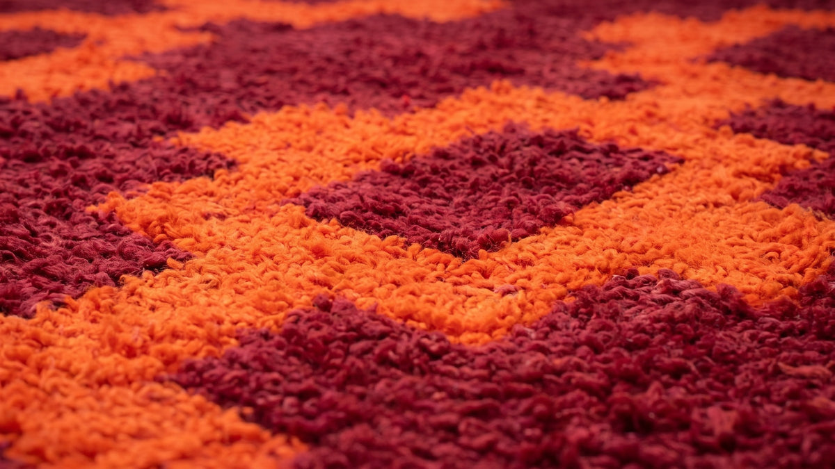 Gros plan sur la laine du tapis berbère Izem, poil bordeaux et orange noué à la main