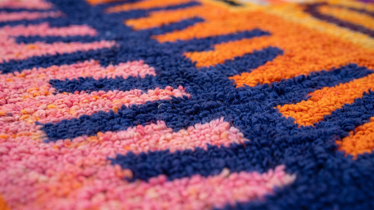Gros plan sur la laine du tapis berbère Tazdayt, poil orange et rose noué à la main