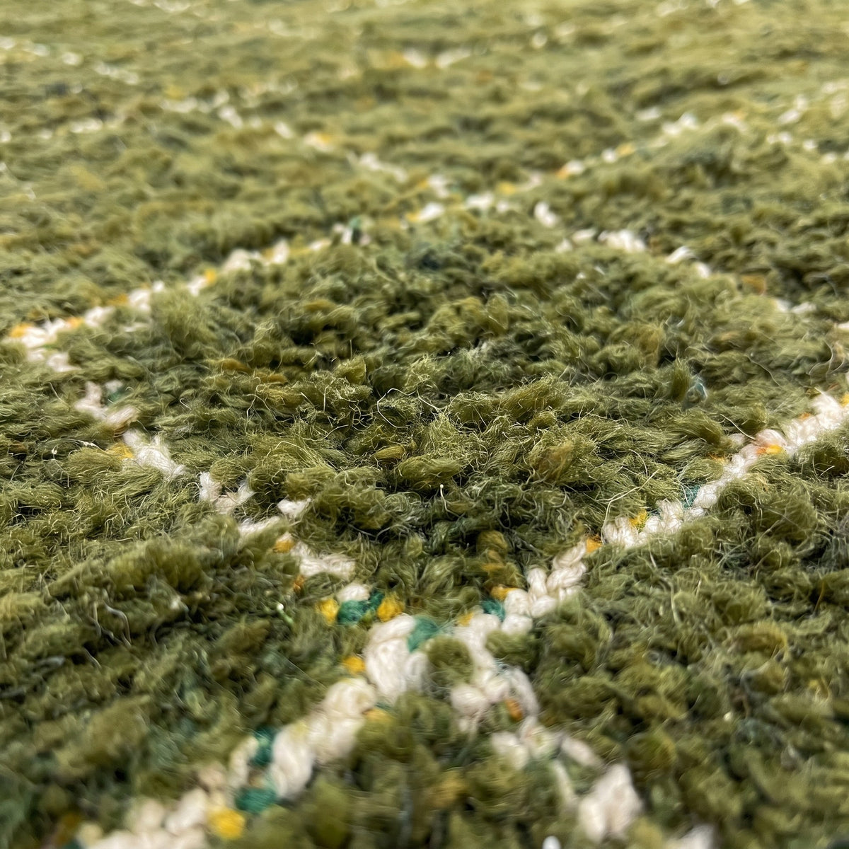 Gros plan sur un motif du tapis berbère Arbaoua, champ vert olive profond quadrillé de fines lignes