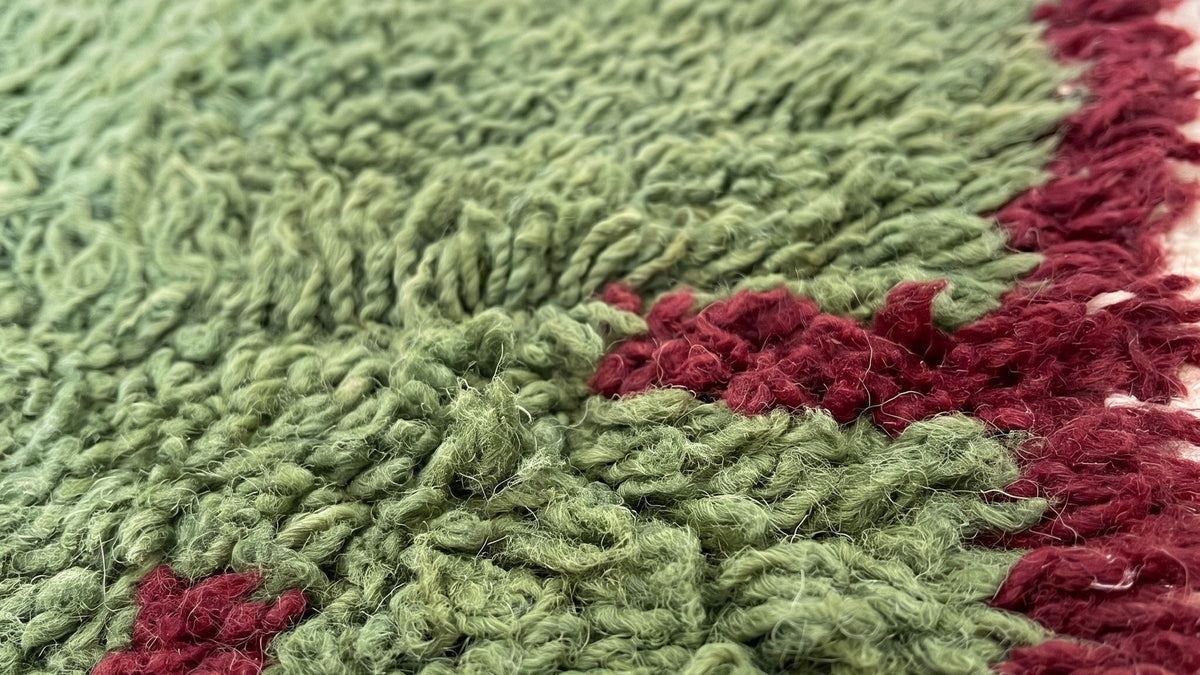 Gros plan sur la laine du tapis berbère Chrafate, poil vert et bordeaux noué à la main