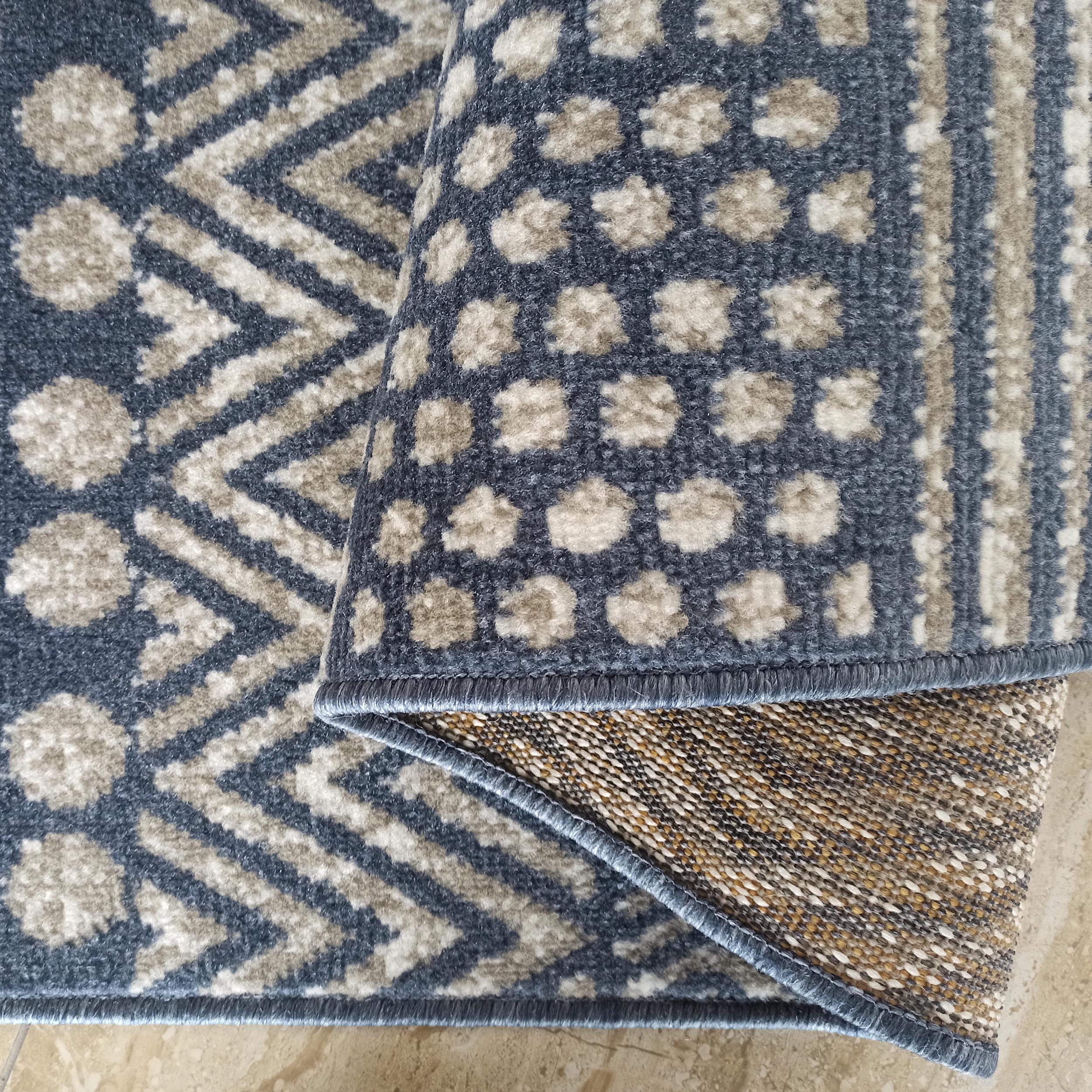 Tapis aux motifs géométriques bleus et beiges, zigzags et formes abstraites, partiellement roulé pour révéler son envers tissé