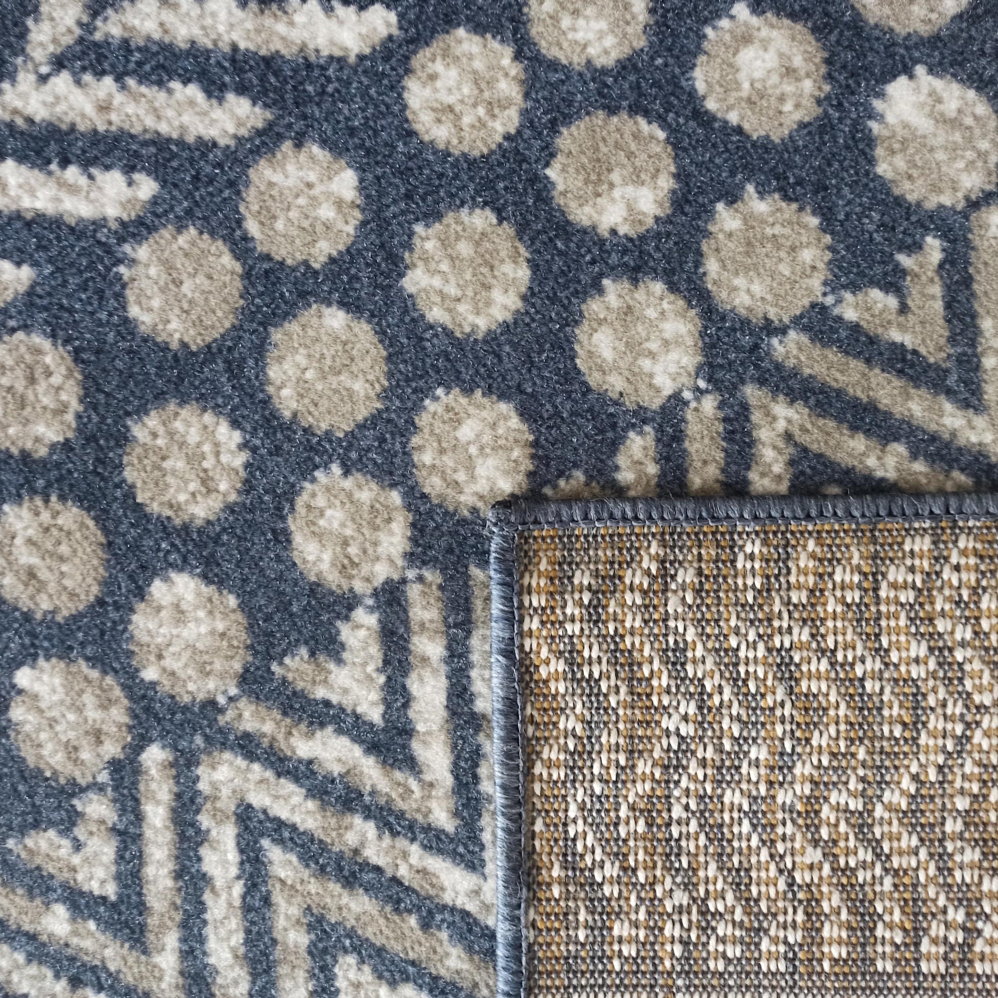 Tapis présentant des motifs géométriques ronds et rayés en beige clair et bleu foncé, avec son envers tissé visible