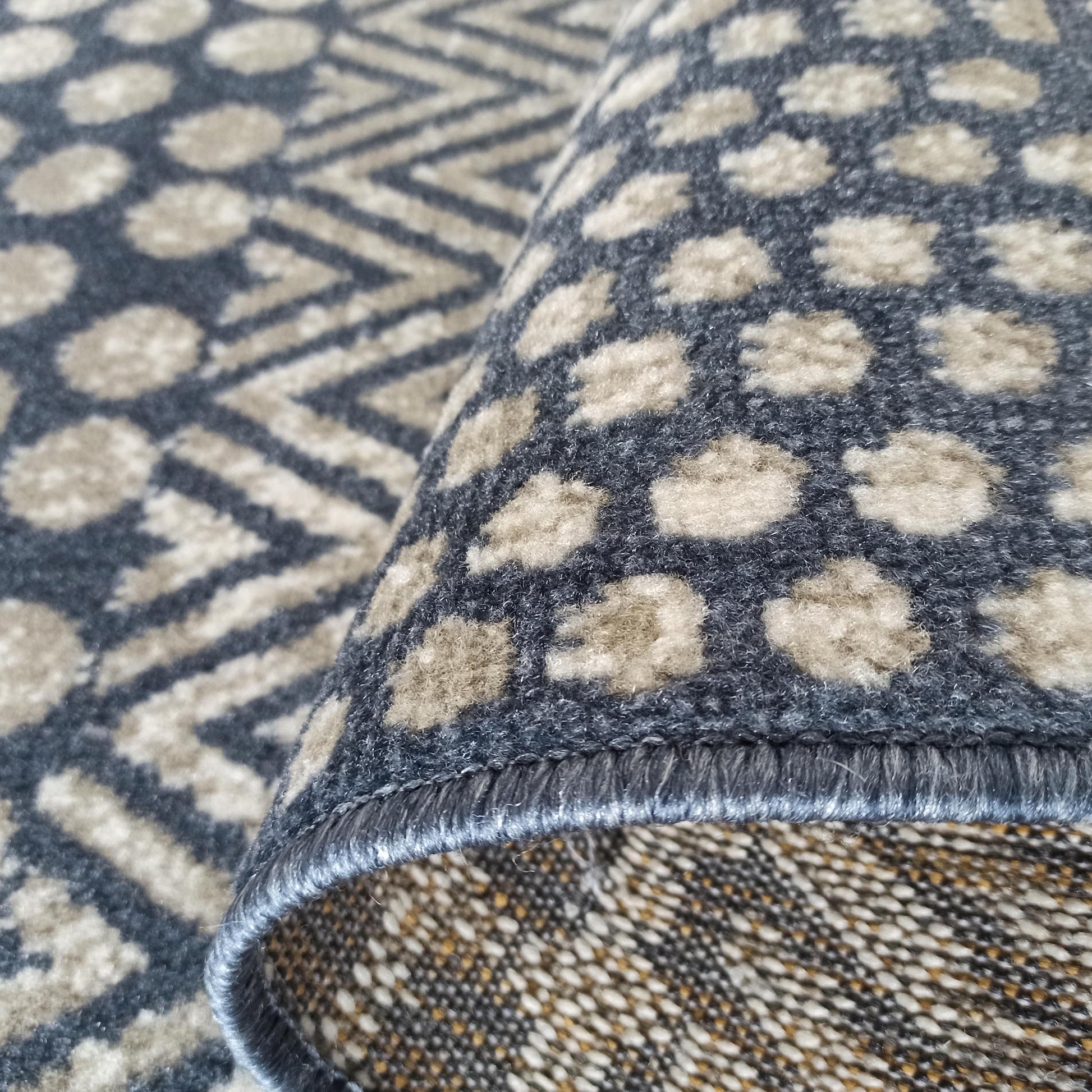 Tapis enroulé présentant un motif de points et de formes géométriques bleu-gris et beige clair, avec sa texture veloutée et son envers tissé