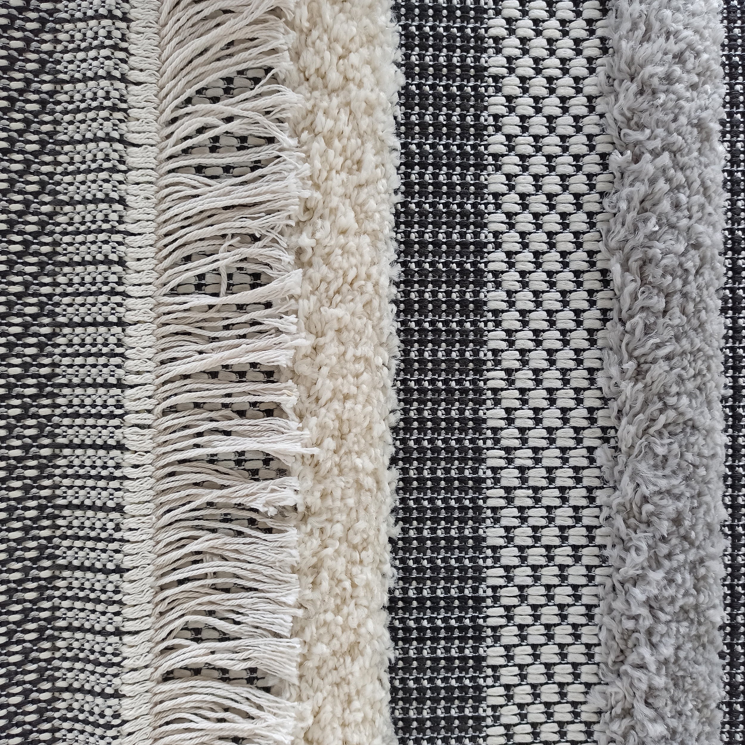Tapis à motifs rayés verticaux mêlant textures tissées en damier noir et blanc, franges claires, et bandes bouclées beige et gris