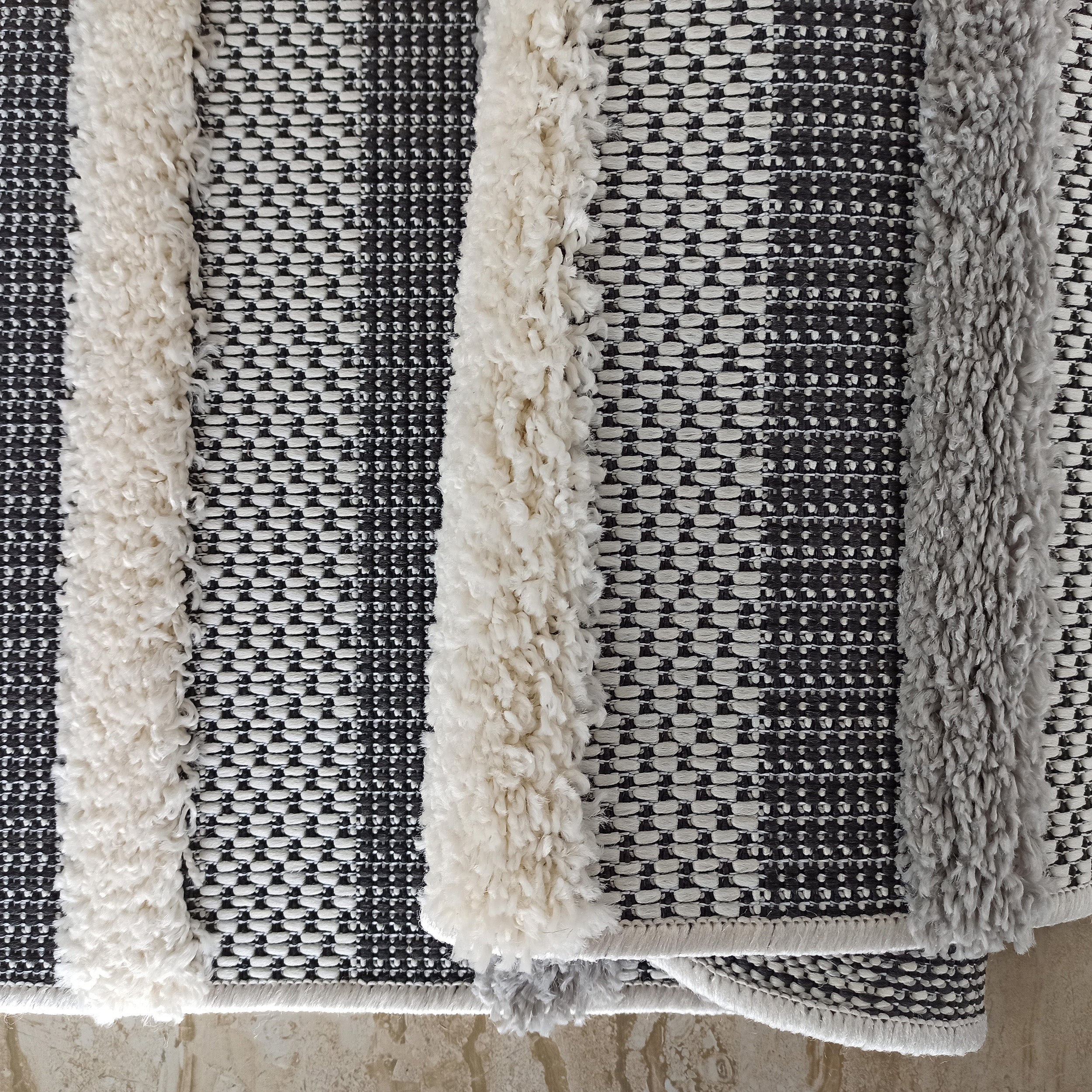 Tapis à rayures verticales, alternant des bandes tissées noires et blanches et des bandes shaggy crème et gris