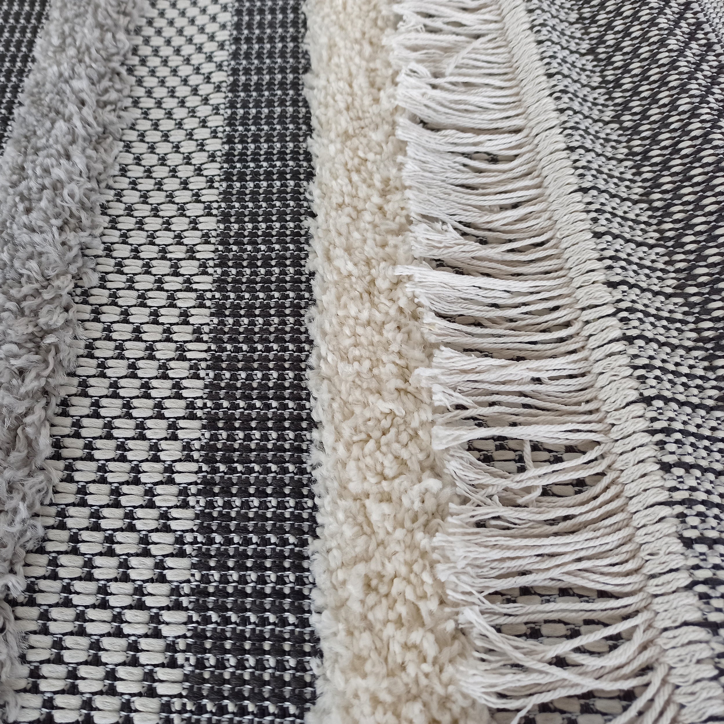 Tapis texturé avec des bandes grises et crème moelleuses, alternant avec des motifs tissés noirs et blancs, et des franges