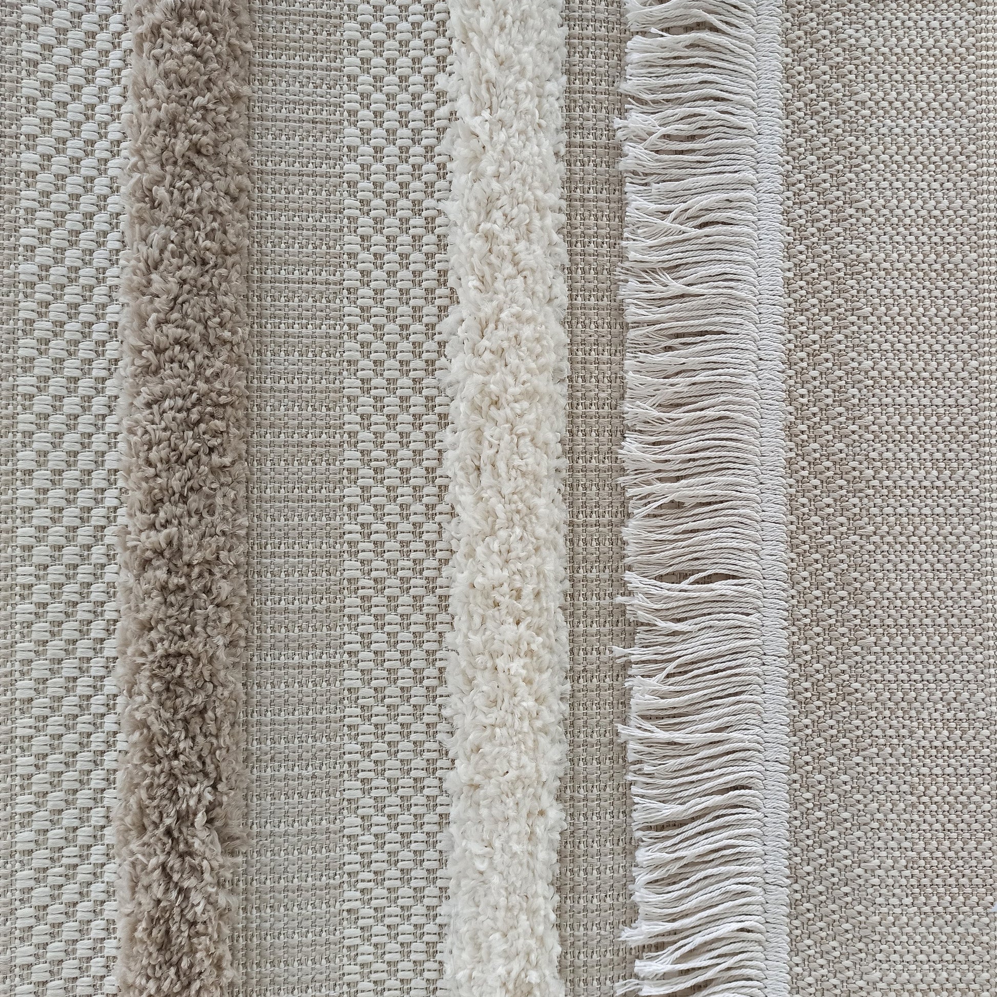 Tapis en tissu texturé beige et écru avec des bandes verticales alternant tressage fin, poil long bouclé et franges