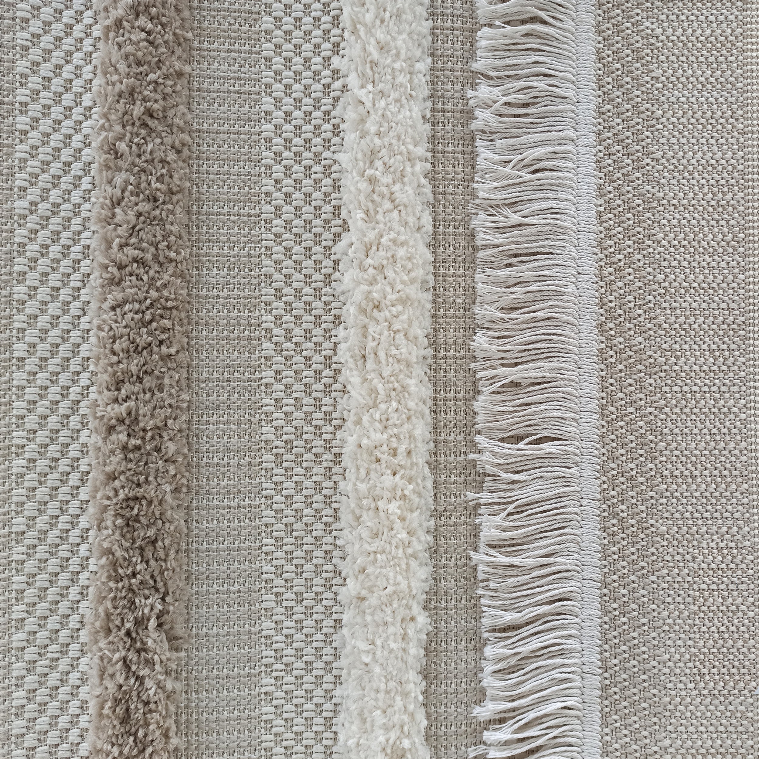 Tapis en tissu texturé beige et écru avec des bandes verticales alternant tressage fin, poil long bouclé et franges