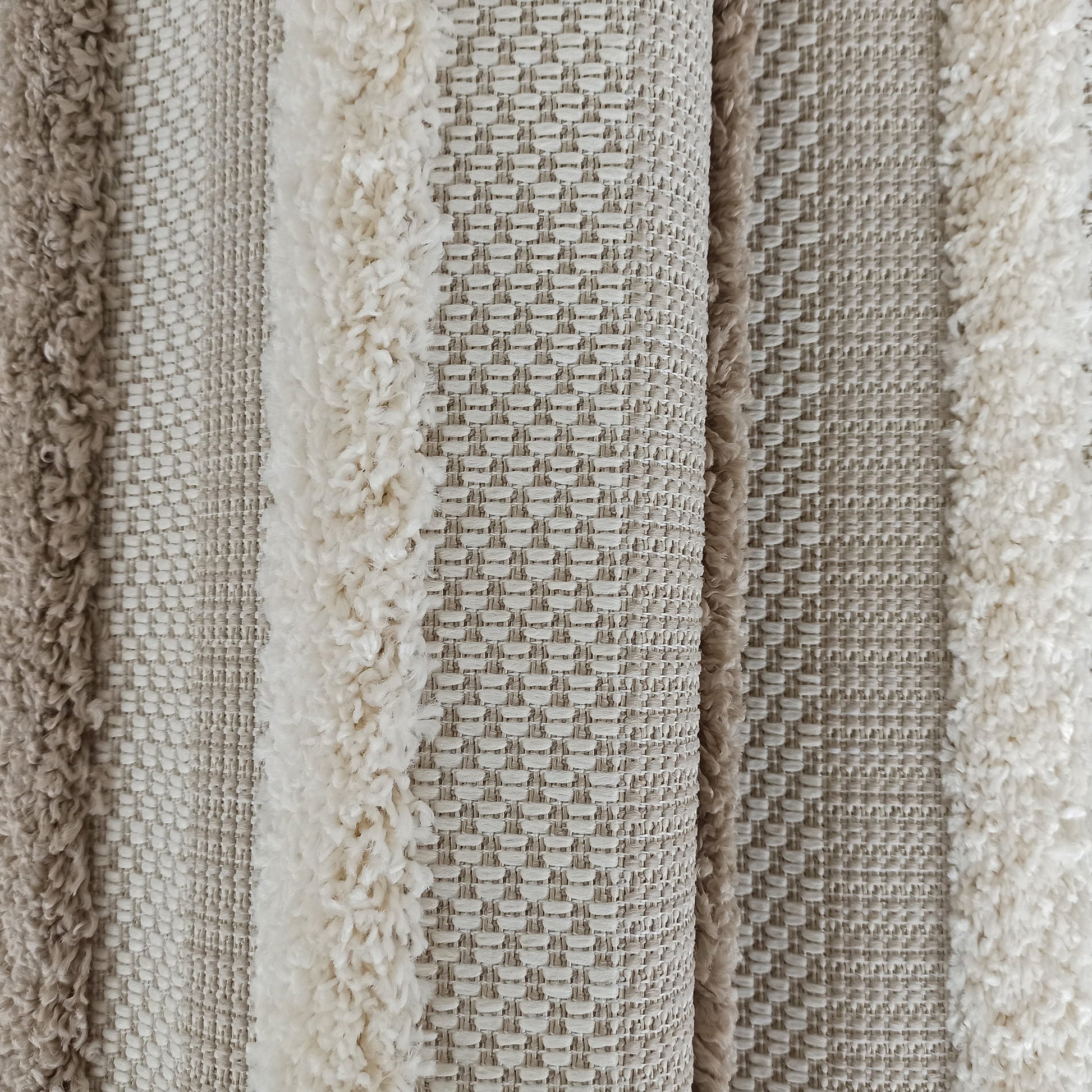 Tapis texturé avec des bandes de couleurs et de textures variées, alternant entre poils longs crème et tissage beige clair