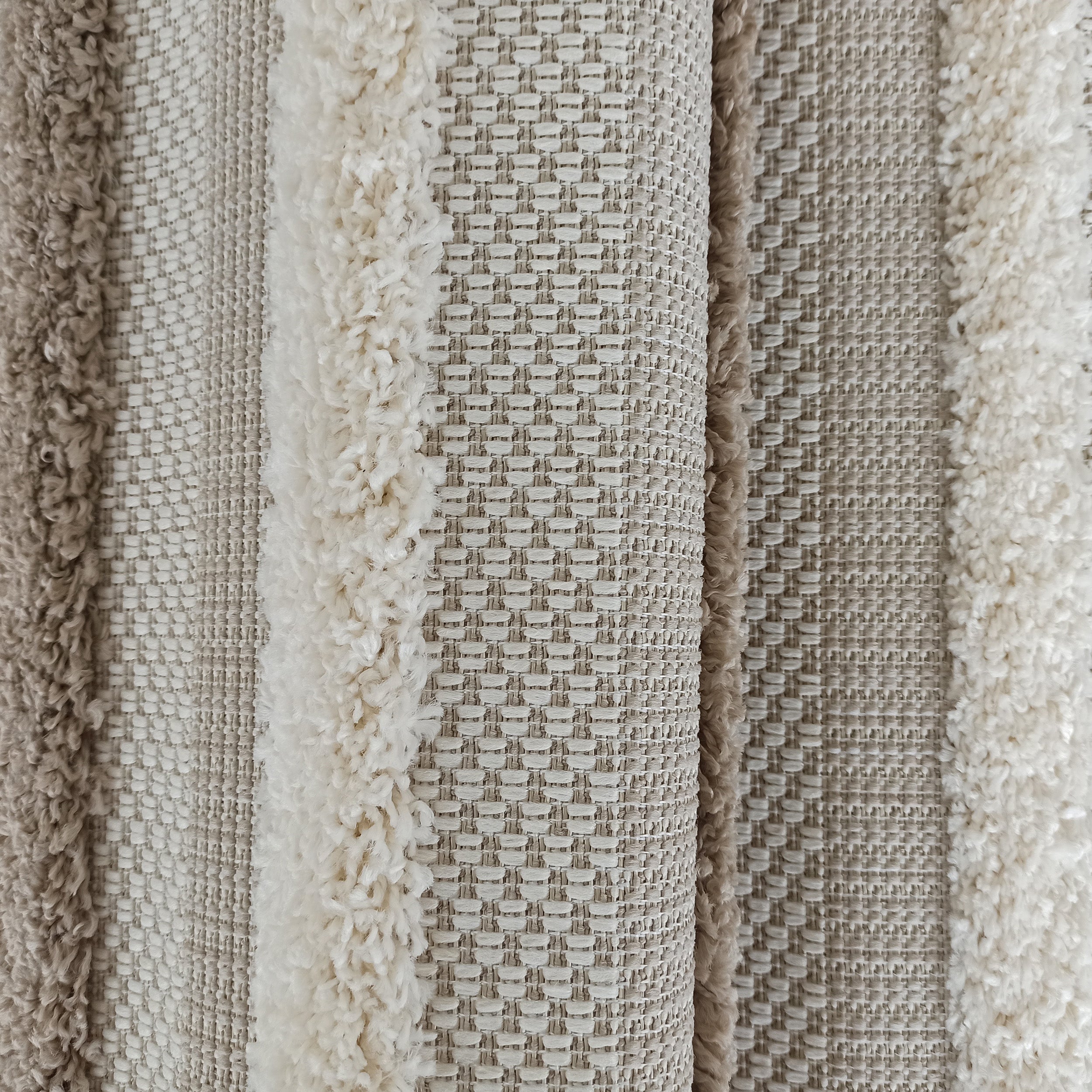 Tapis texturé avec des bandes de couleurs et de textures variées, alternant entre poils longs crème et tissage beige clair