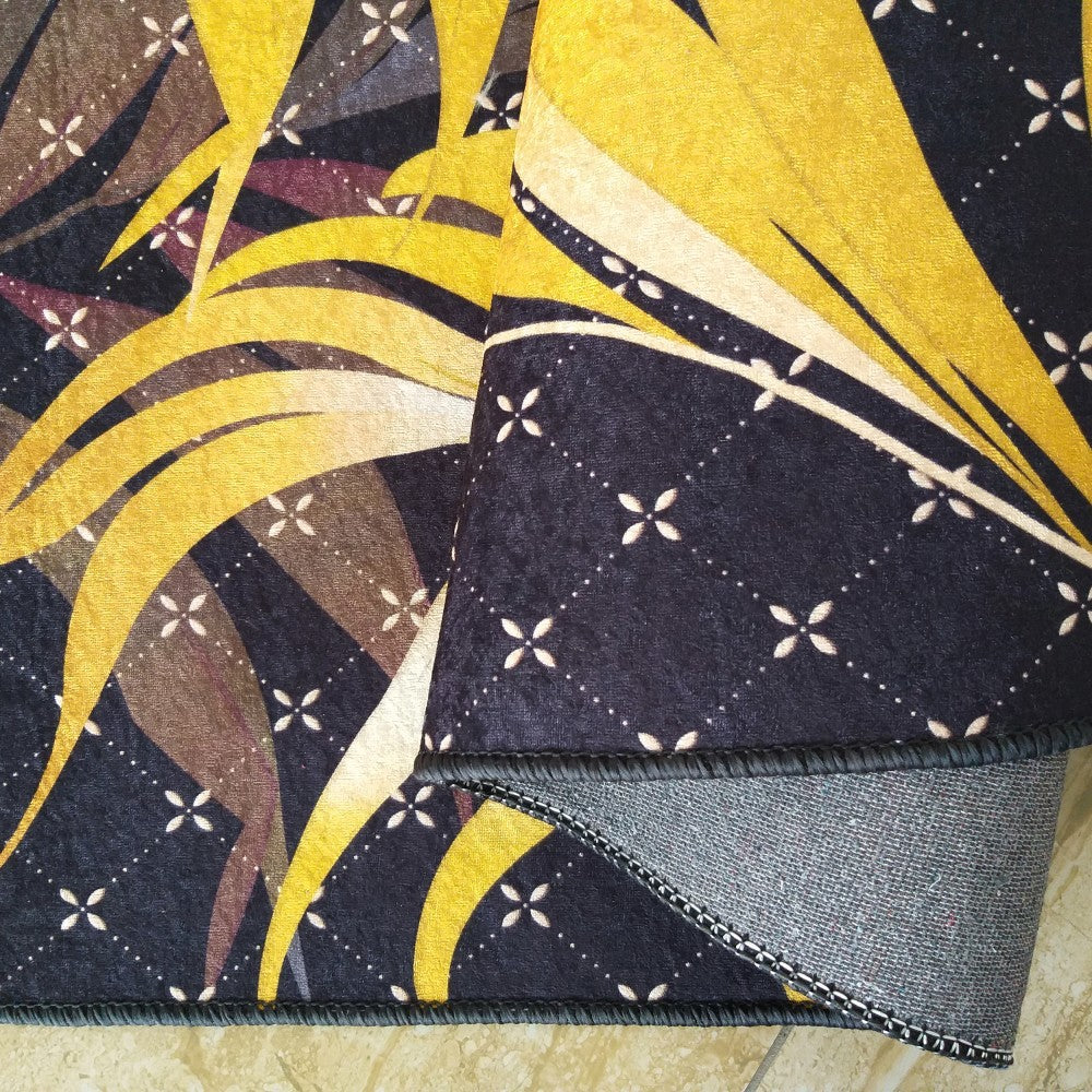 Tapis jaune et or aux grands motifs de feuilles et petits motifs floraux blancs sur fond noir, sa sous-face grise est visible