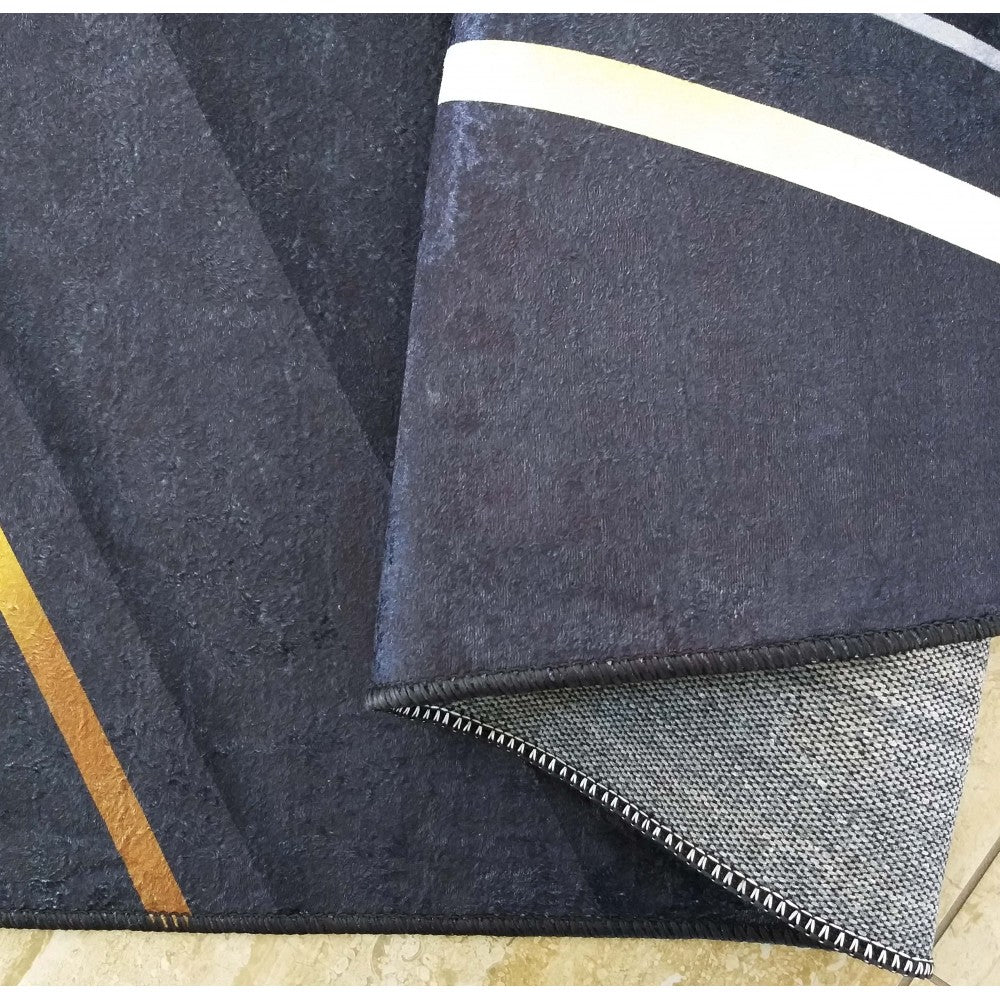 Tapis foncé avec des motifs géométriques, une bande dorée à gauche et une bande blanche à droite. Le tapis est partiellement plié, montrant son envers gris et son ourlet noir