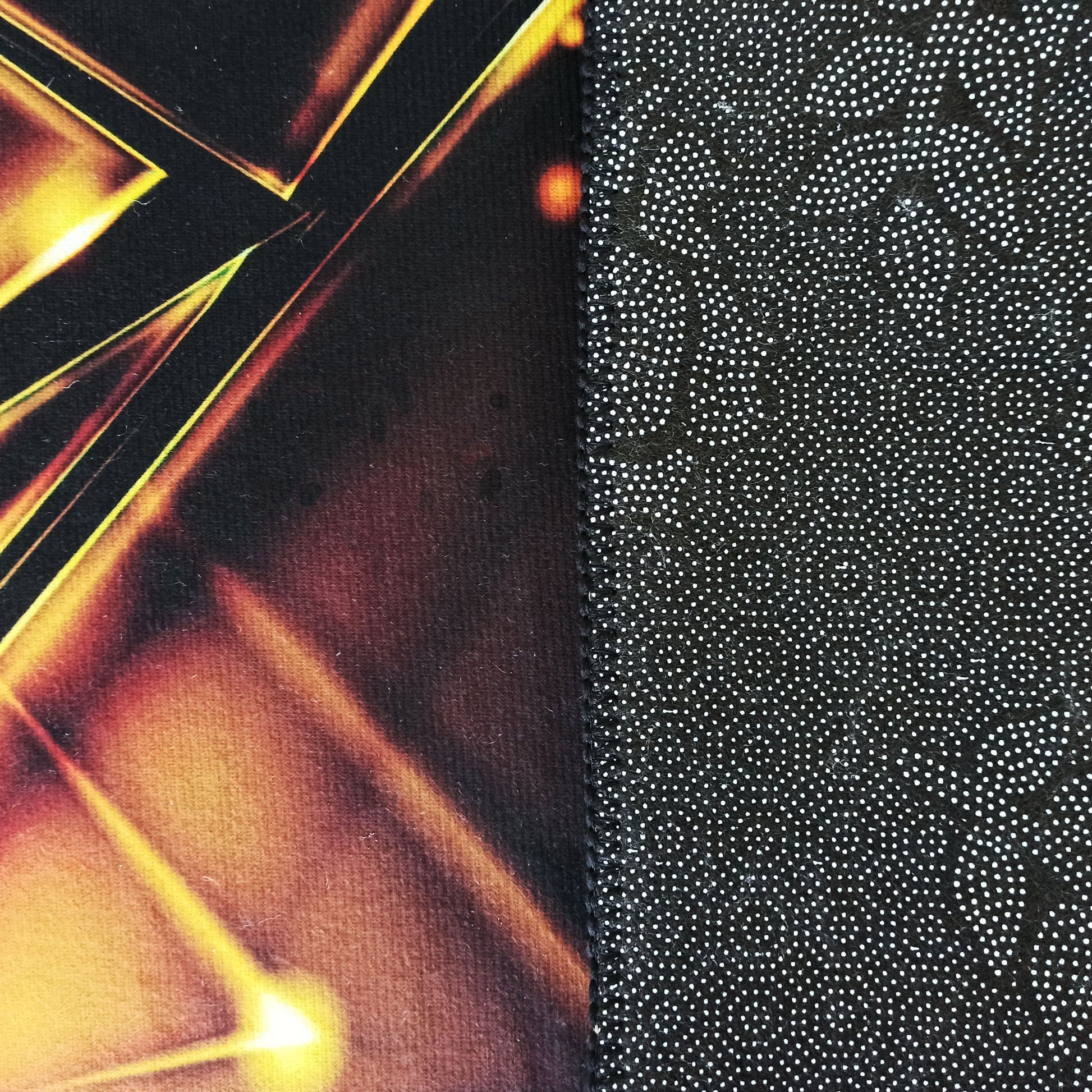 Gros plan d'un tapis montrant le dessus avec un motif abstrait jaune et orange sur fond foncé et le dessous noir à pois blancs antidérapants