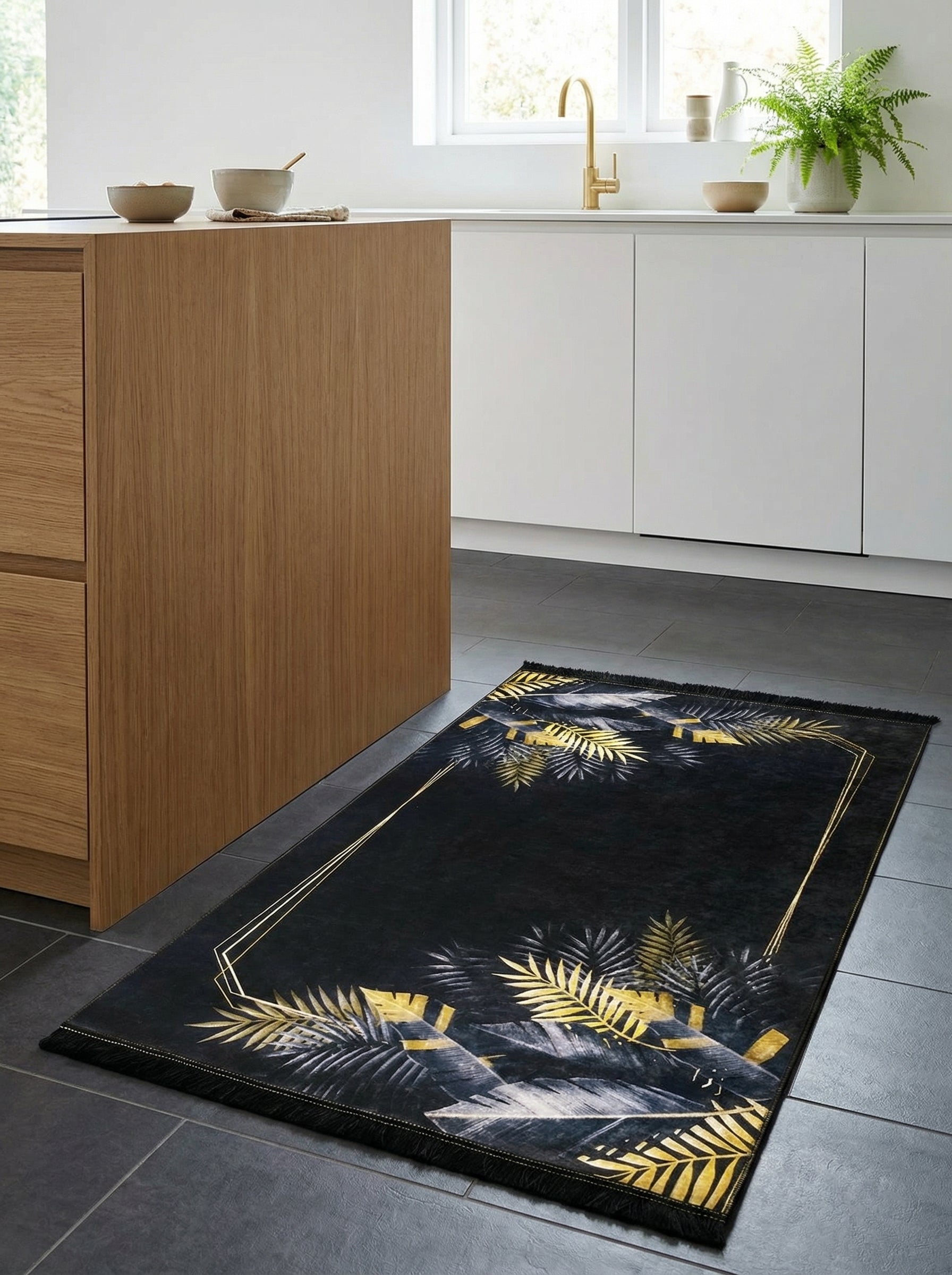 Tapis rectangulaire noir orné de palmes dorées et gris-bleu, avec un cadre géométrique doré et des franges, posé dans une cuisine moderne