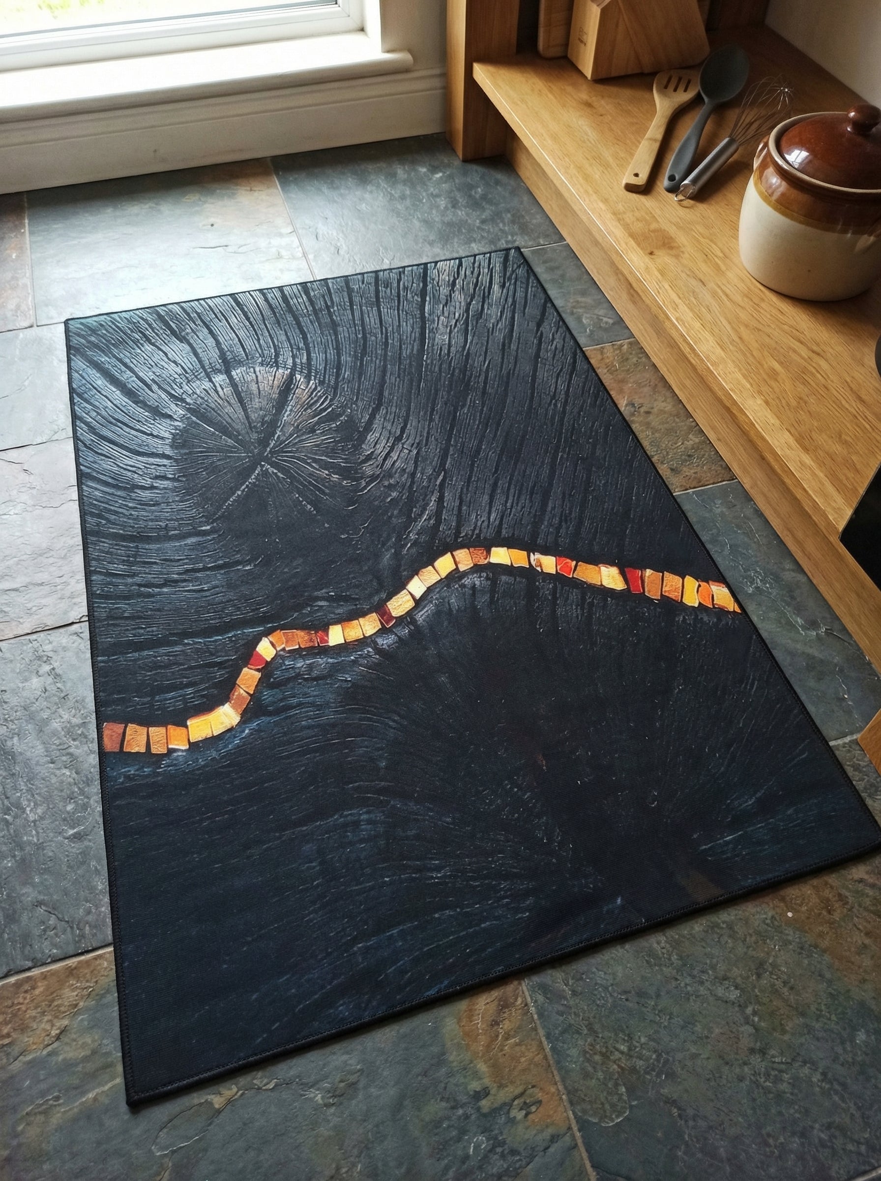 Tapis rectangulaire sombre effet bois cerné, avec une ligne sinueuse de carrés lumineux orange-rouge, sur un carrelage foncé de cuisine
