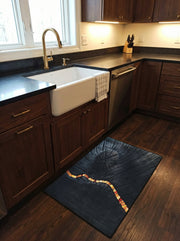 Tapis rectangulaire noir texturé avec un motif circulaire et une ligne sinueuse de fragments orange et or, dans une cuisine