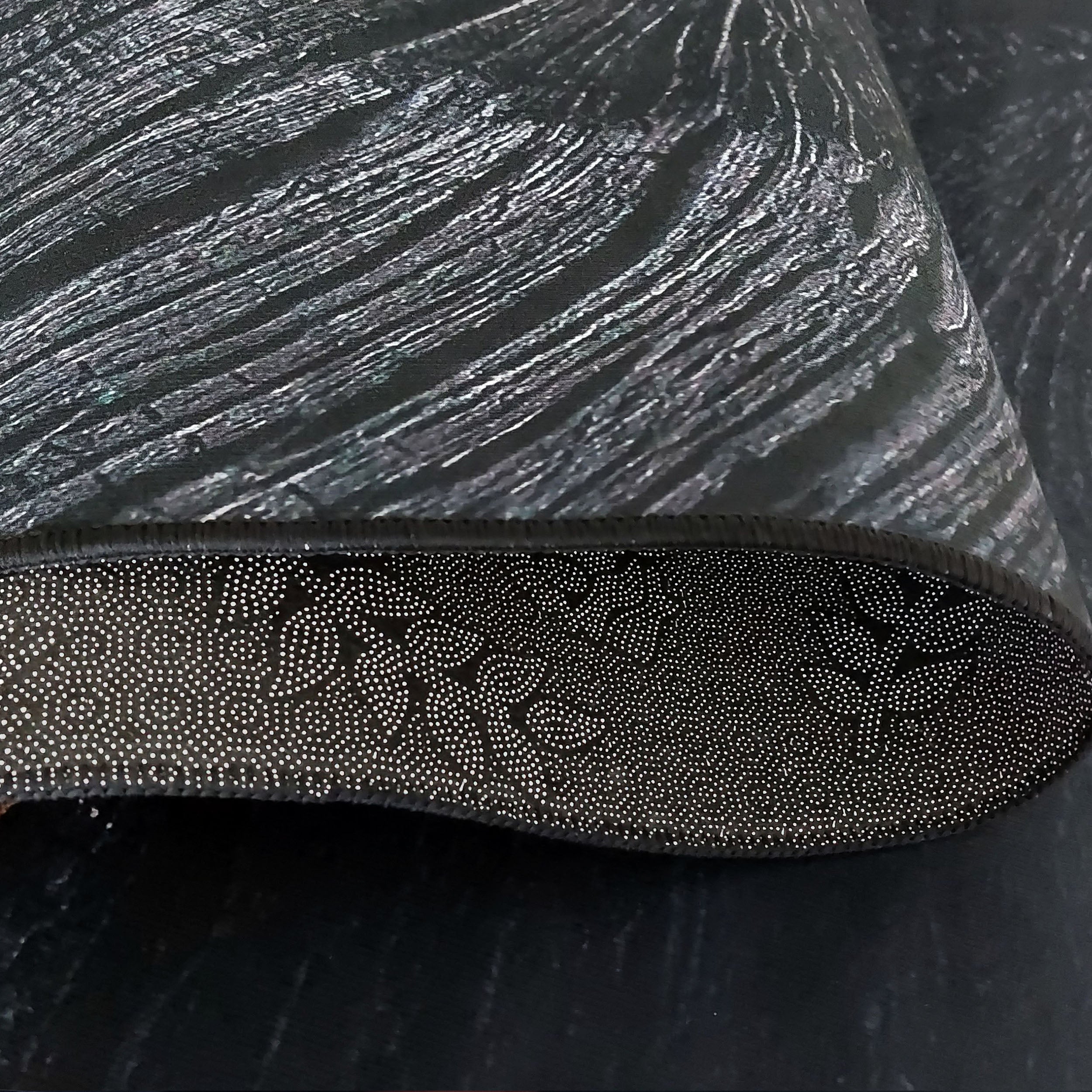 Tapis noir à texture striée gris argenté, l'envers visible présente un motif antidérapant de points blancs en spirales