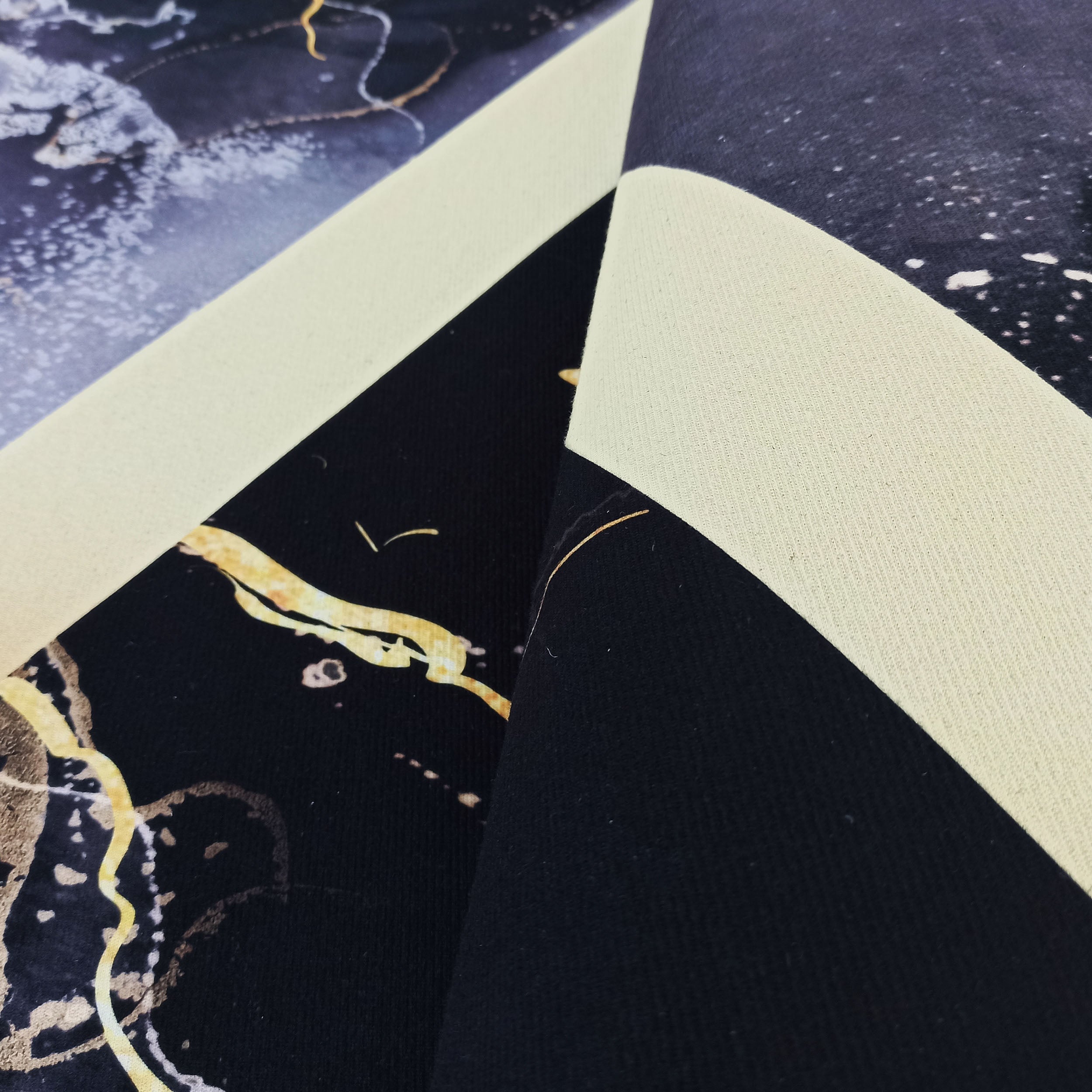 Tapis avec un motif abstrait marbré en bleu foncé, noir, blanc et doré, montrant son envers uni crème à la texture tissée