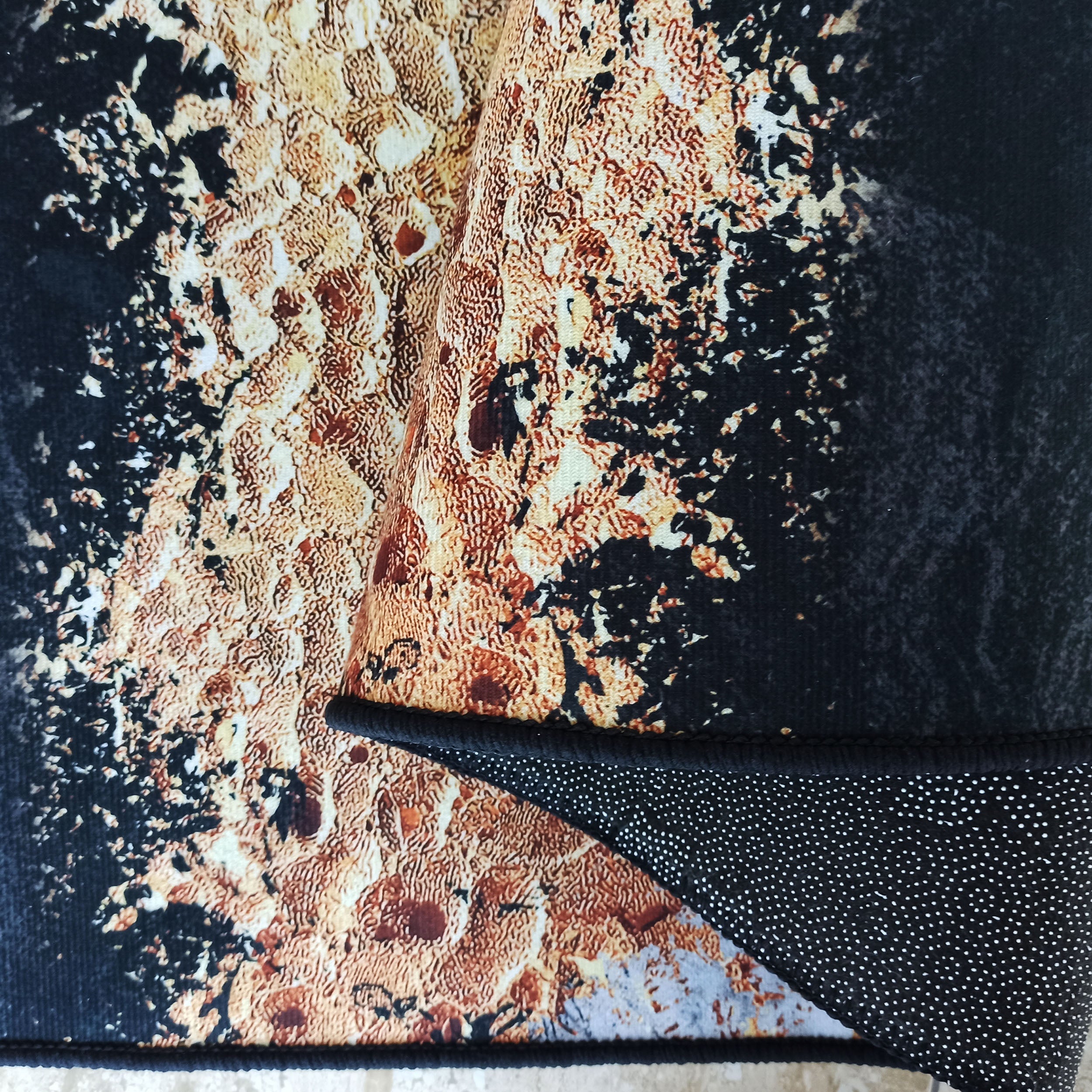 Tapis aux motifs abstraits et texturés noir, orange rouille et crème, dont l'envers antidérapant noir à points blancs est exposé