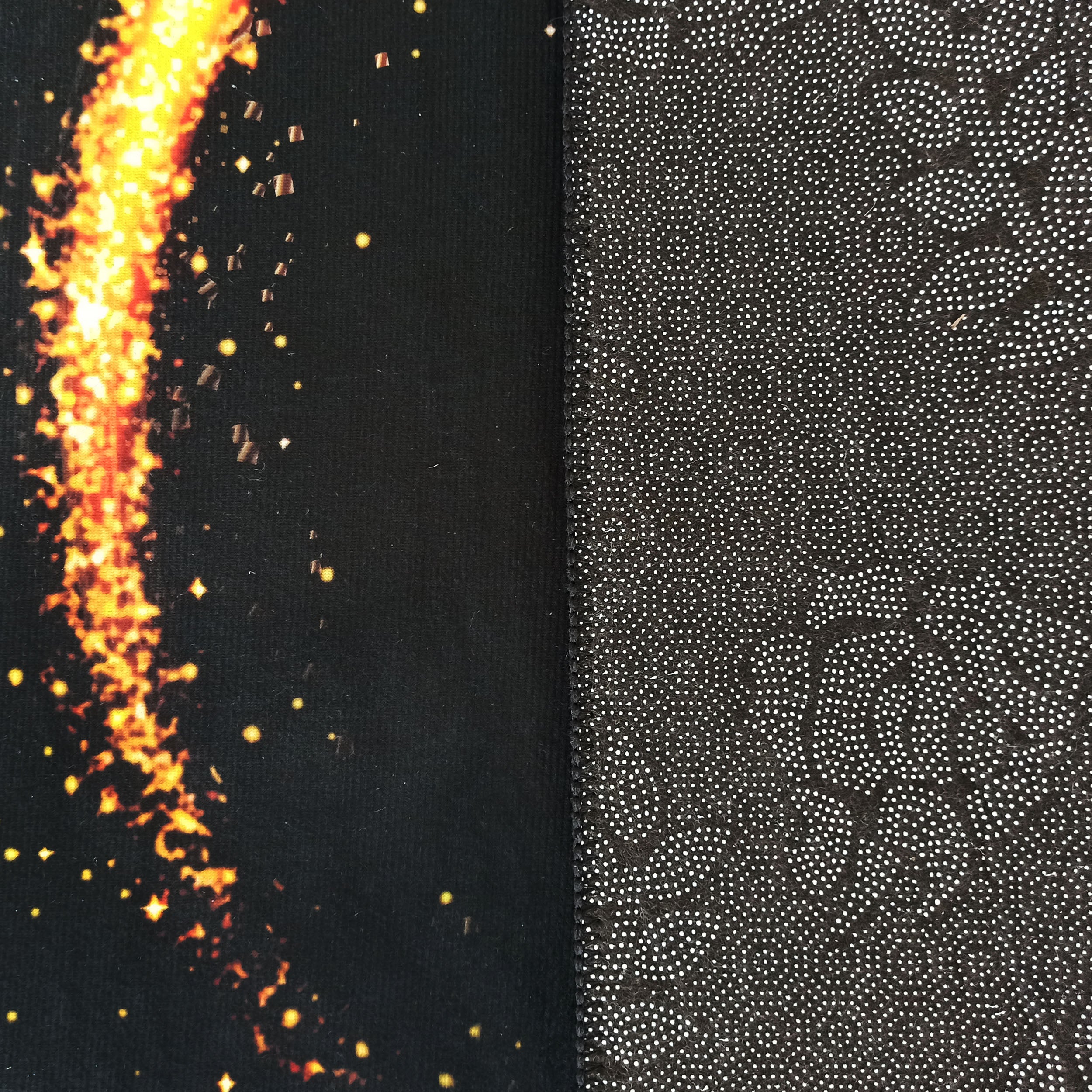 Tapis dont le dessus noir présente un motif flamboyant orange et jaune, et le dessous sombre est parsemé de pois blancs