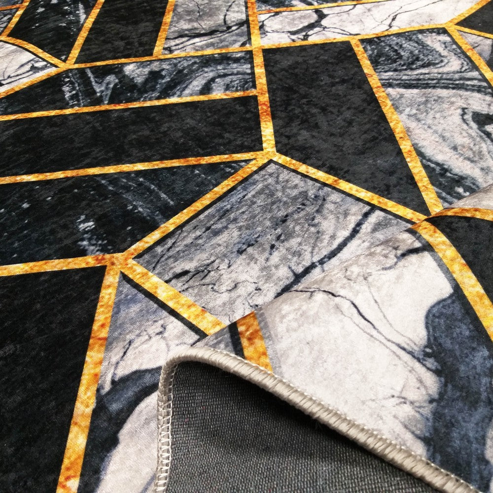 Tapis à motifs géométriques noir et gris marbré, avec des lignes dorées et le bord surjeté révélant le dessous sombre