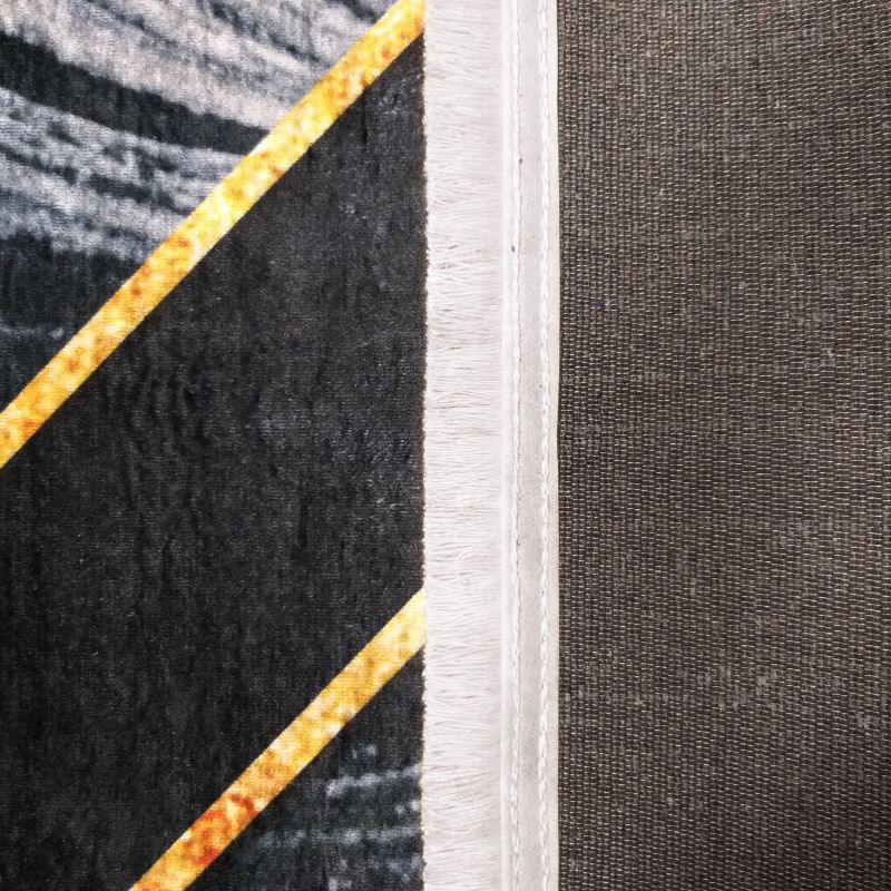 Gros plan d'un tapis doux à motifs géométriques noirs, dorés et gris clair, avec frange blanche et dos tissé sombre