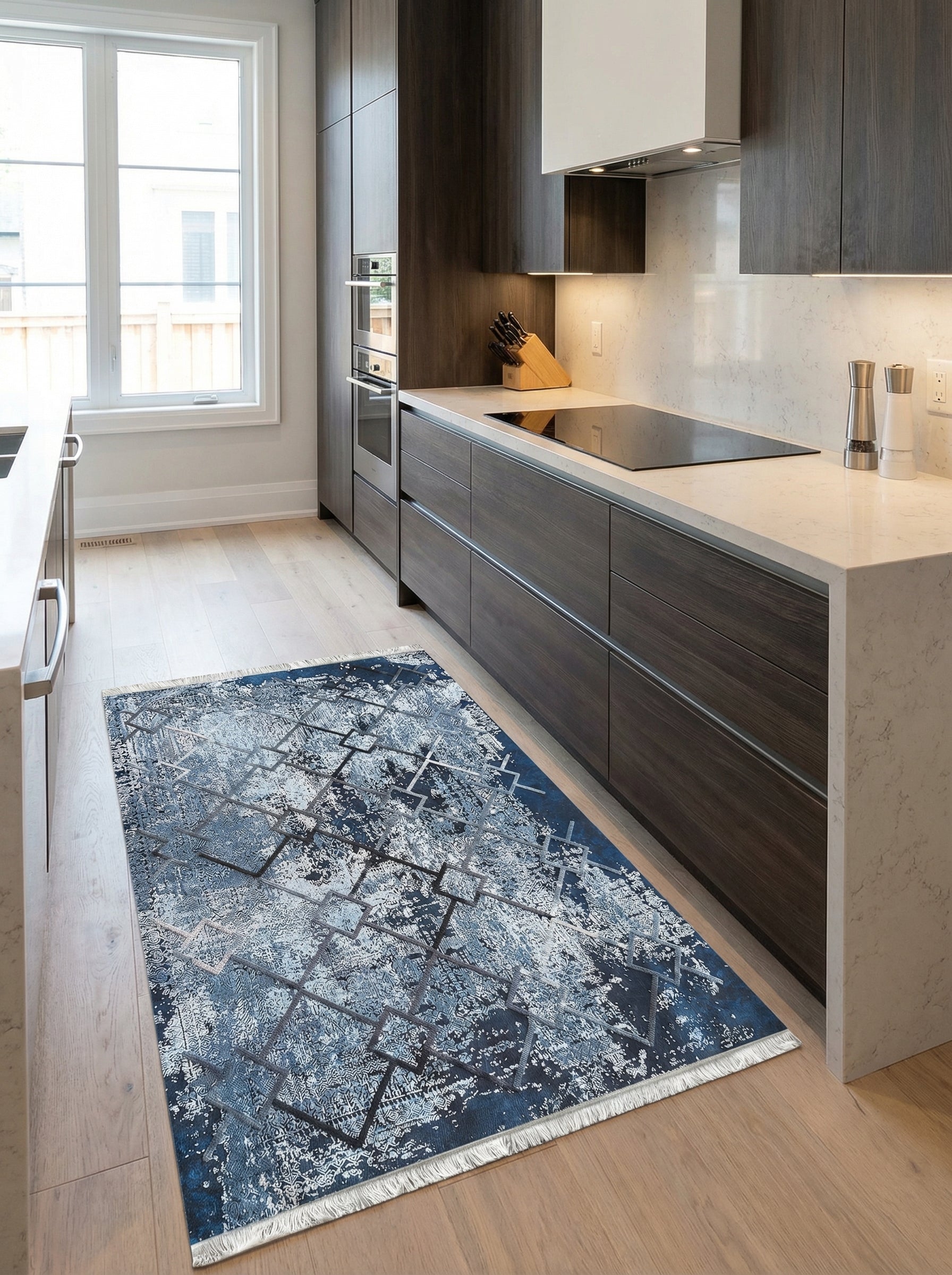 Tapis rectangulaire bleu marine et gris aux motifs géométriques abstraits et usés, avec franges, dans une cuisine moderne au sol en bois clair