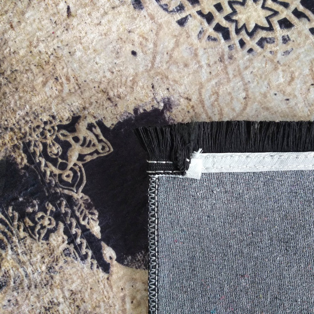Gros plan sur un tapis à la texture douce, présentant des motifs ornementaux noirs sur fond beige, avec des franges noires et le revers gris visible