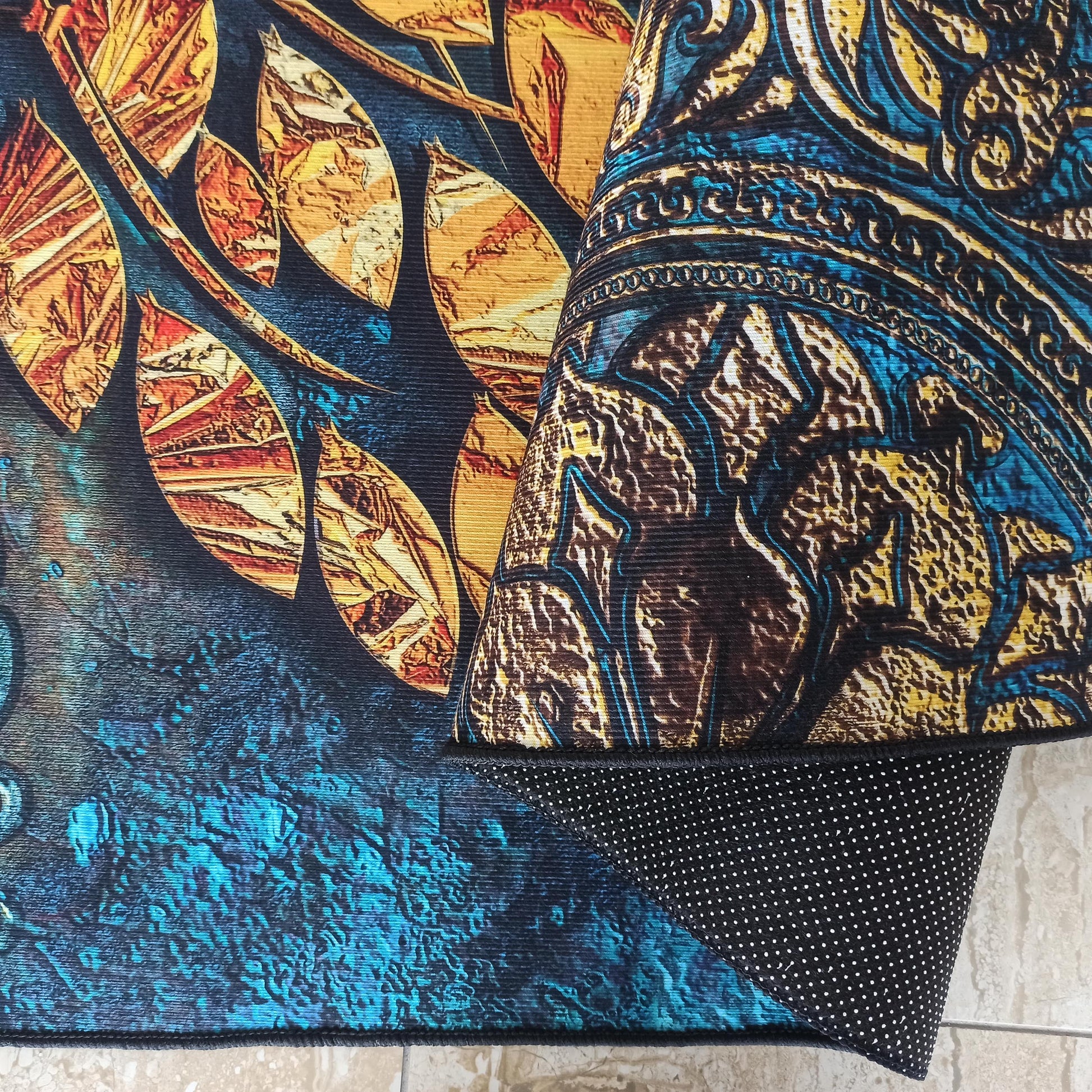 Tapis à motifs de feuilles orange, jaunes et bleues, un second tapis enroulé révèle des motifs bleus, jaunes et bruns avec un envers noir à pois blancs