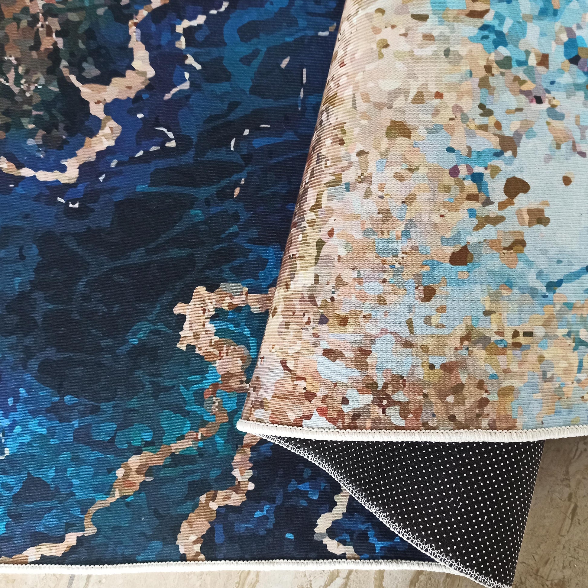 Tapis à motifs abstraits, bleu foncé, beige, marron clair et bleu ciel. Son dessous est noir à pois blancs
