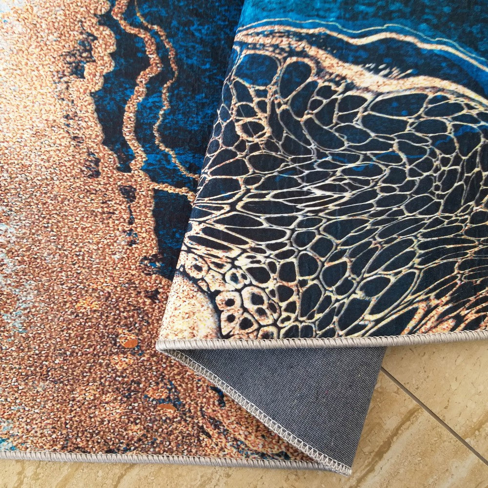 Tapis partiellement roulé aux motifs abstraits bleus, noirs et ocre, avec textures sableuses et formes cellulaires, son revers étant gris et ourlé