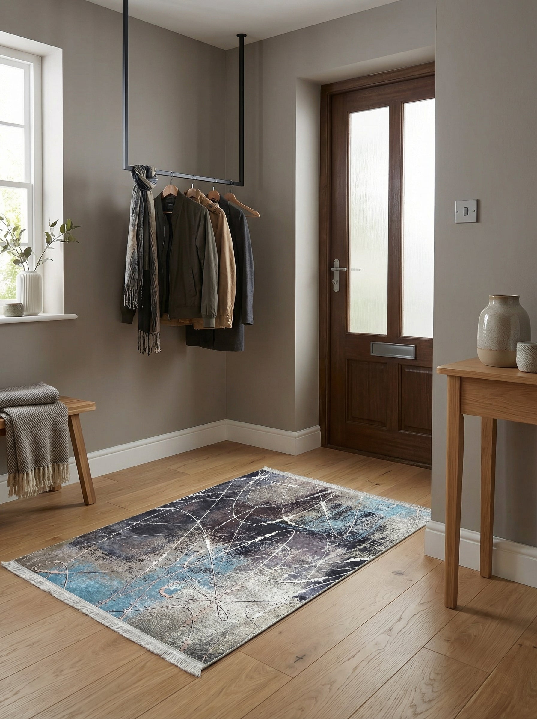 Tapis rectangulaire abstrait aux motifs de taches et lignes blanches, bleues, grises et sombres, posé sur un parquet clair dans une entrée