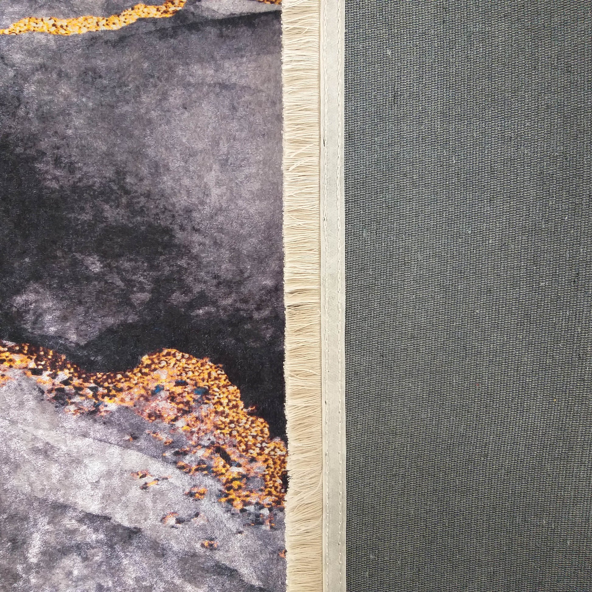 Tapis à surface veloutée gris foncé et clair aux motifs abstraits dorés, bordé de franges crème et envers tissé gris