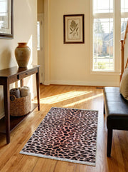 Tapis rectangulaire imprimé léopard beige rosé et taches sombres, avec franges, sur un parquet clair d'entrée