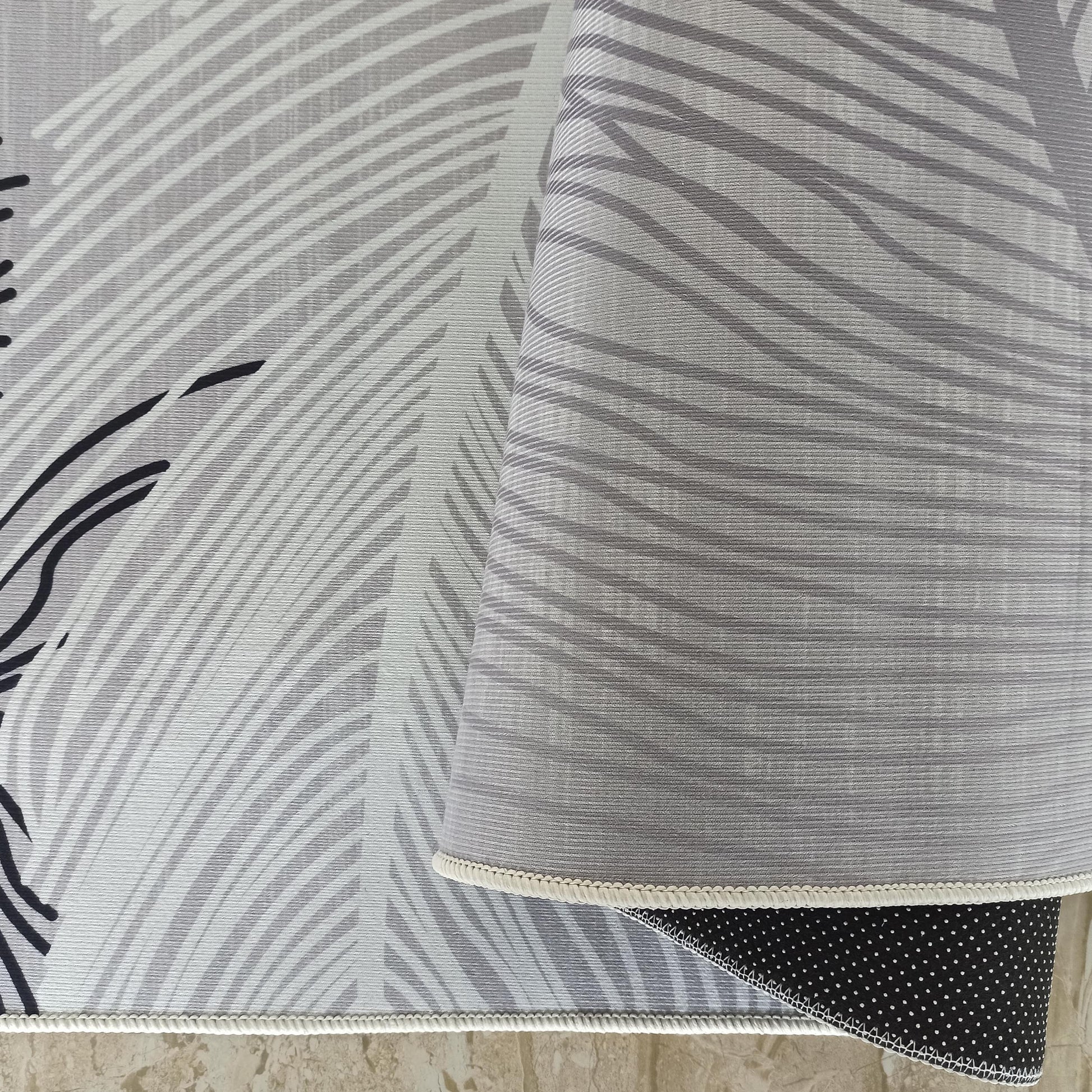 Tapis gris aux motifs abstraits blancs et noirs, surface côtelée visible, bordure tressée et envers noir à pois blancs