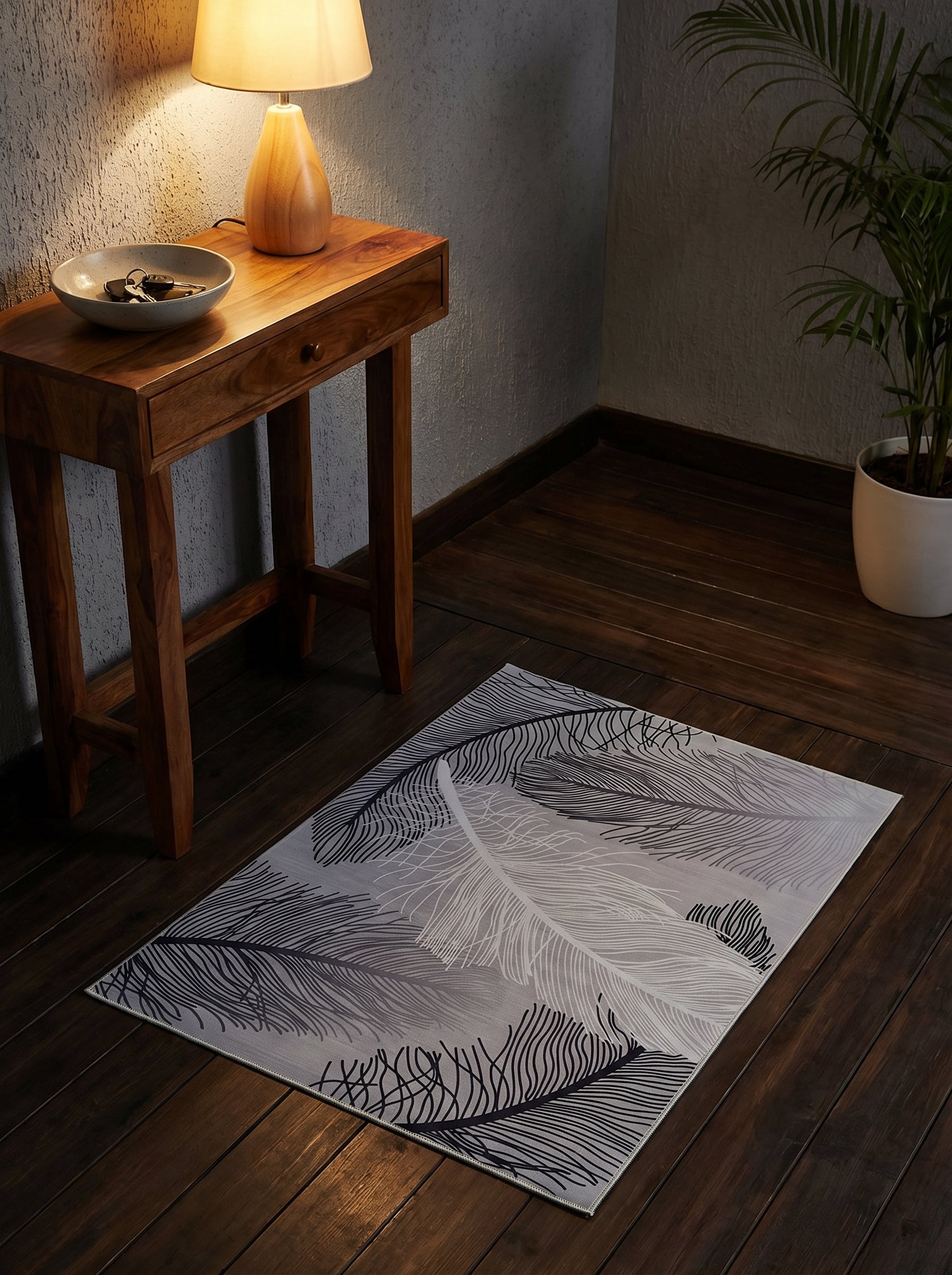Tapis rectangulaire gris clair orné de grands motifs de plumes noires et blanches sur un sol en bois foncé dans une entrée