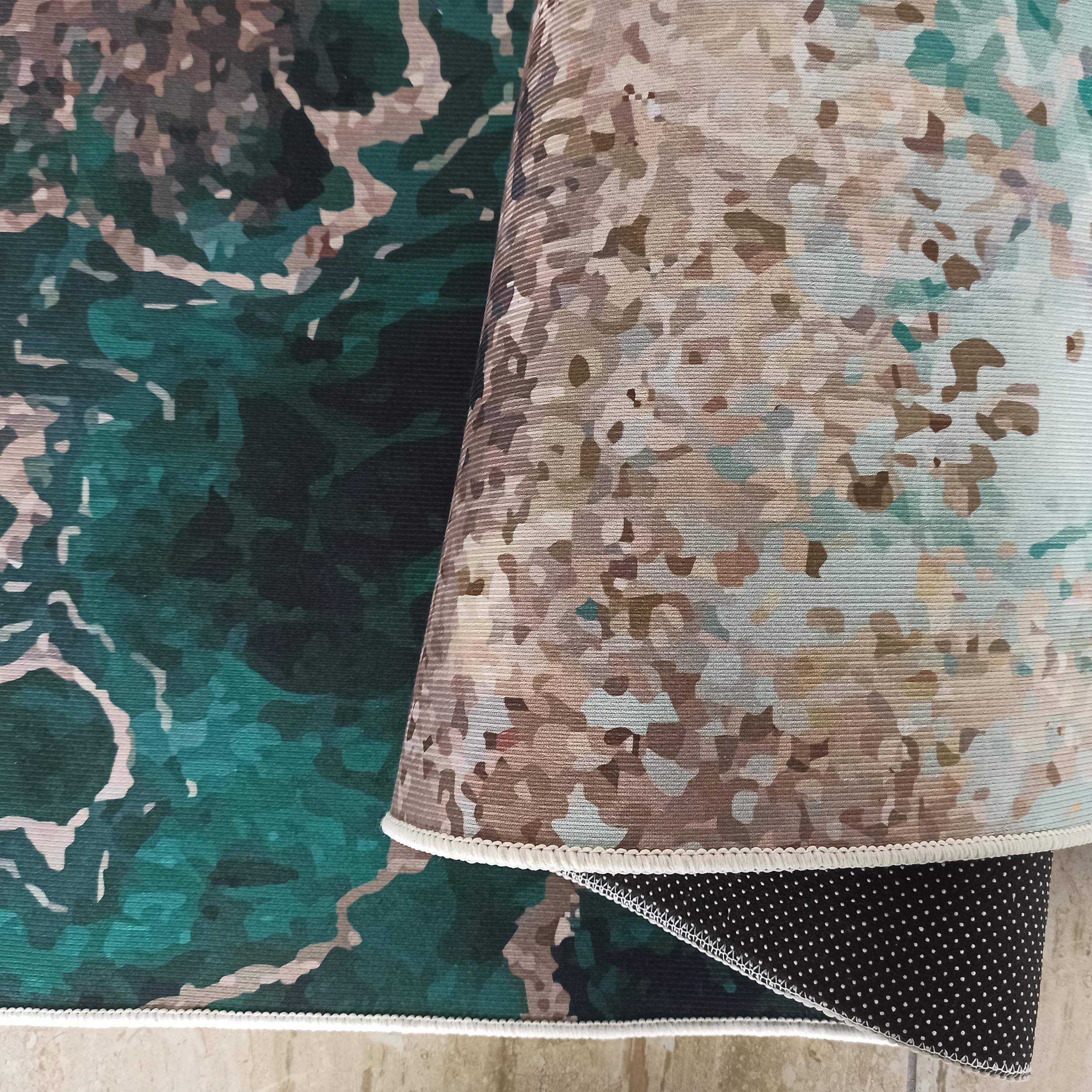 Deux tapis colorés à motifs abstraits. Un tapis vert et turquoise est recouvert par un tapis beige et marron clair plié, dont l'envers noir antidérapant à pois blancs est visible