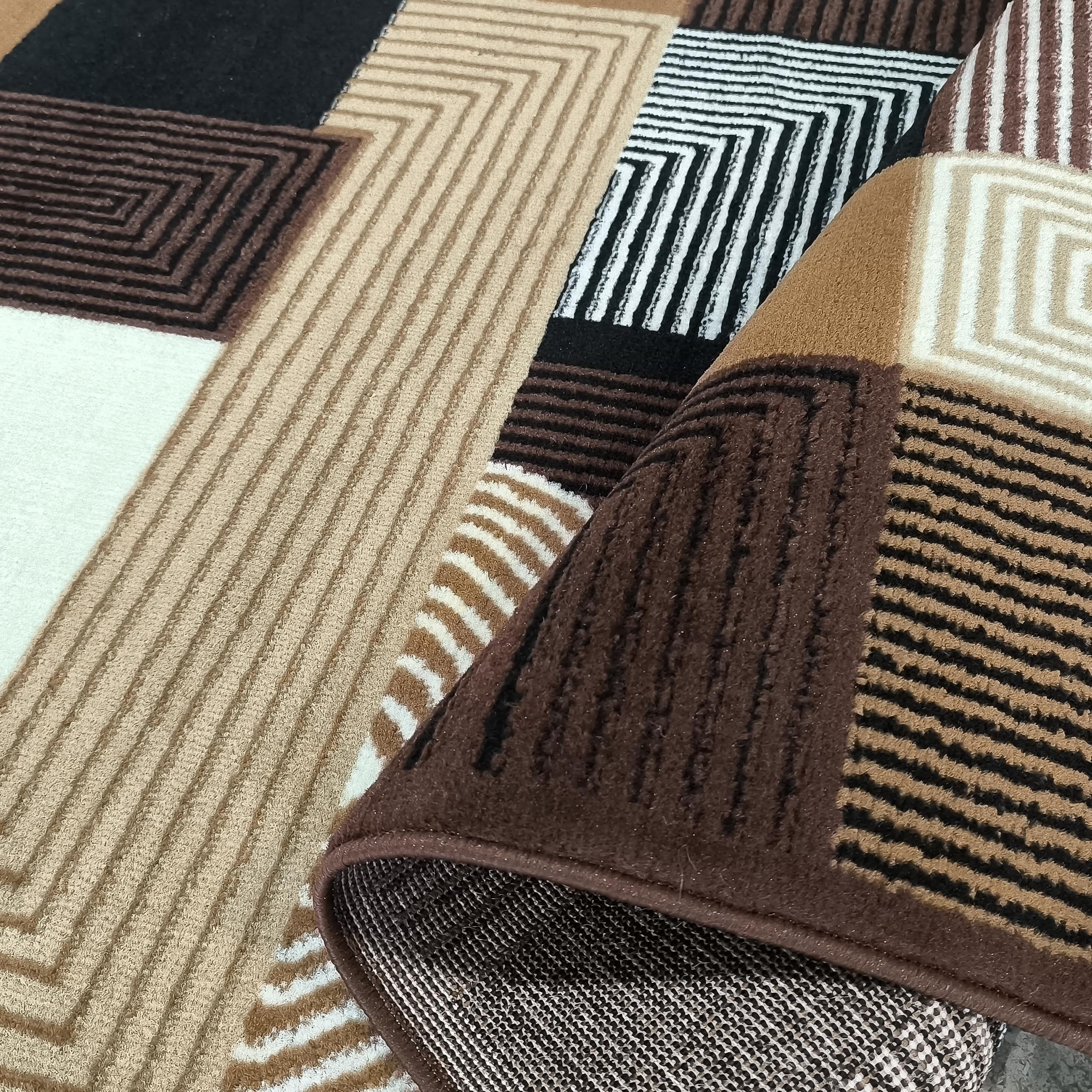 Tapis avec des motifs géométriques en marron, beige, noir et blanc crème. Une section est repliée, révélant l'envers tissé