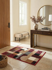 Tapis rectangulaire à motifs géométriques complexes en rouge foncé, noir, beige et crème sur le sol d'une entrée moderne