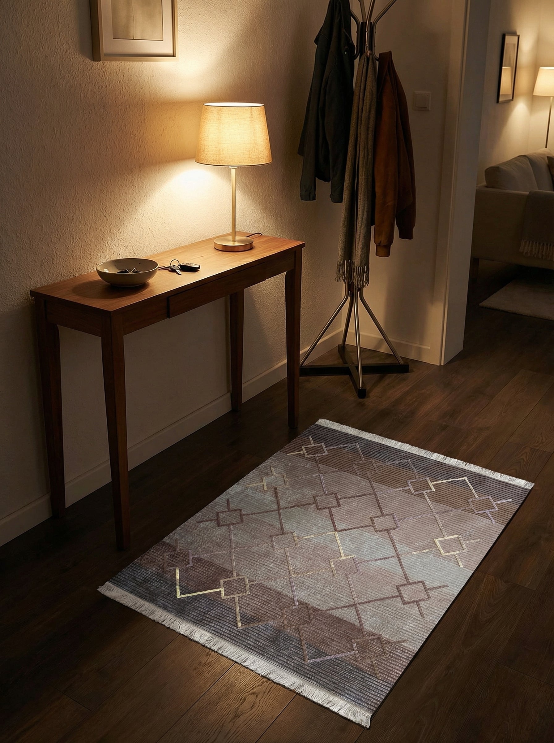 Tapis aux dégradés de gris et brun-mauve, orné de motifs géométriques dorés et clairs. Il est posé sur un parquet dans une entrée