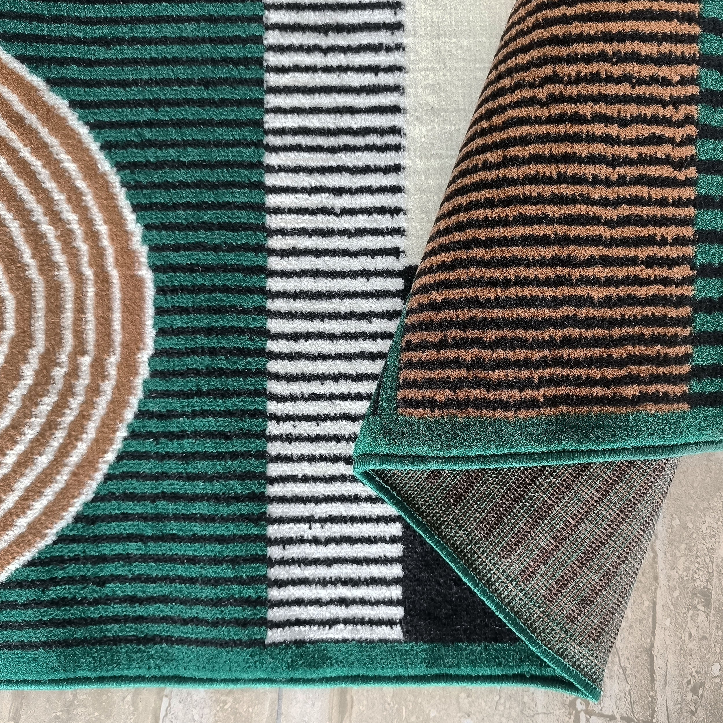 Tapis à motifs géométriques vert, noir, blanc et marron clair, avec une section enroulée