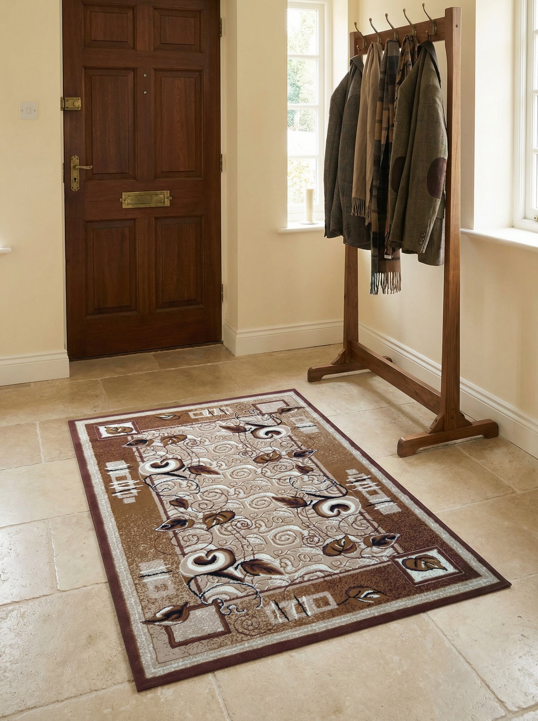 Tapis rectangulaire aux motifs végétaux volutes marron et beiges sur fond clair, bordure foncée, dans une entrée avec carrelage clair